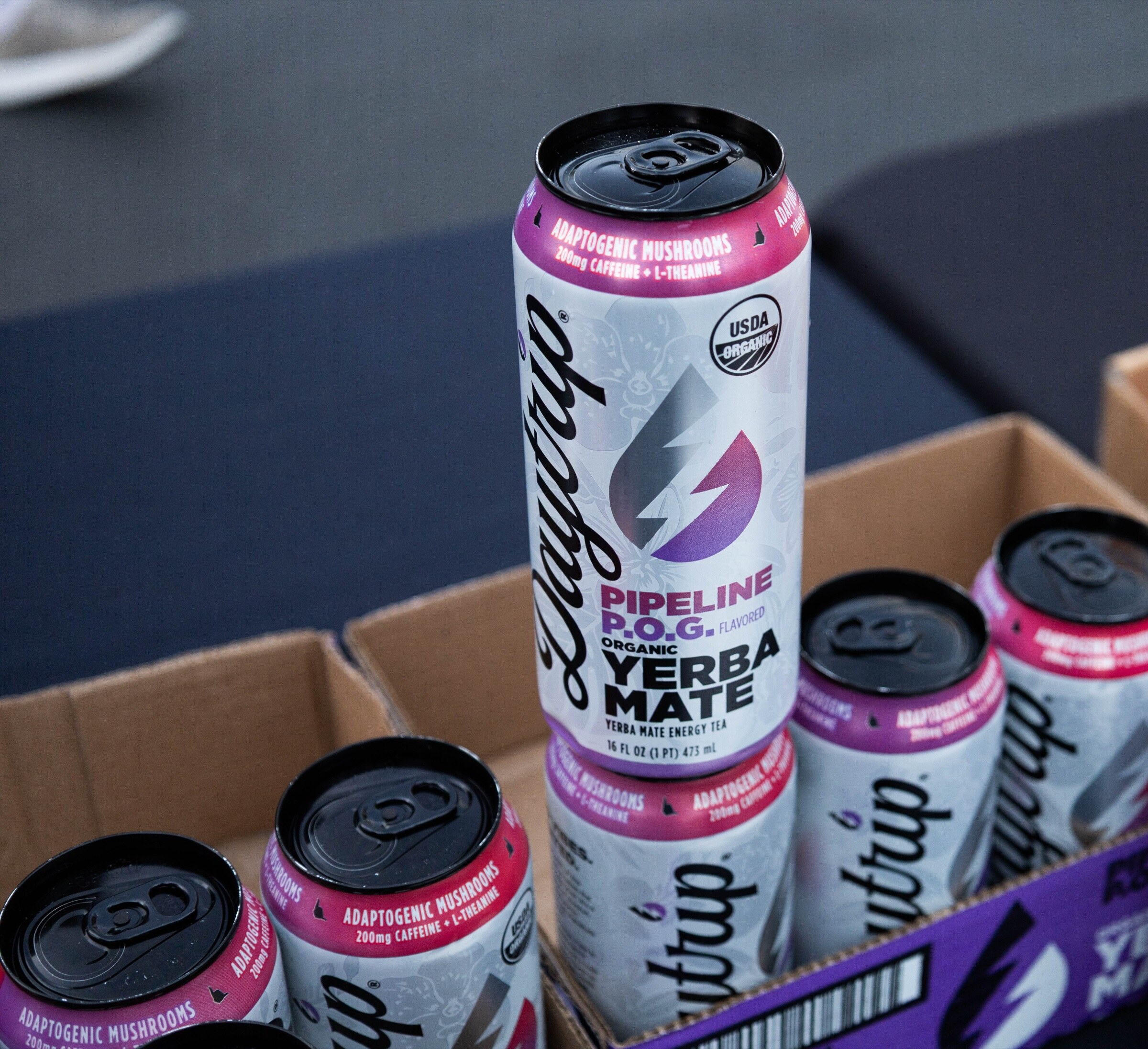 A can of Daytrip Pipeline P.O.G. organic yerba mate standing on a case of Daytrip cans.