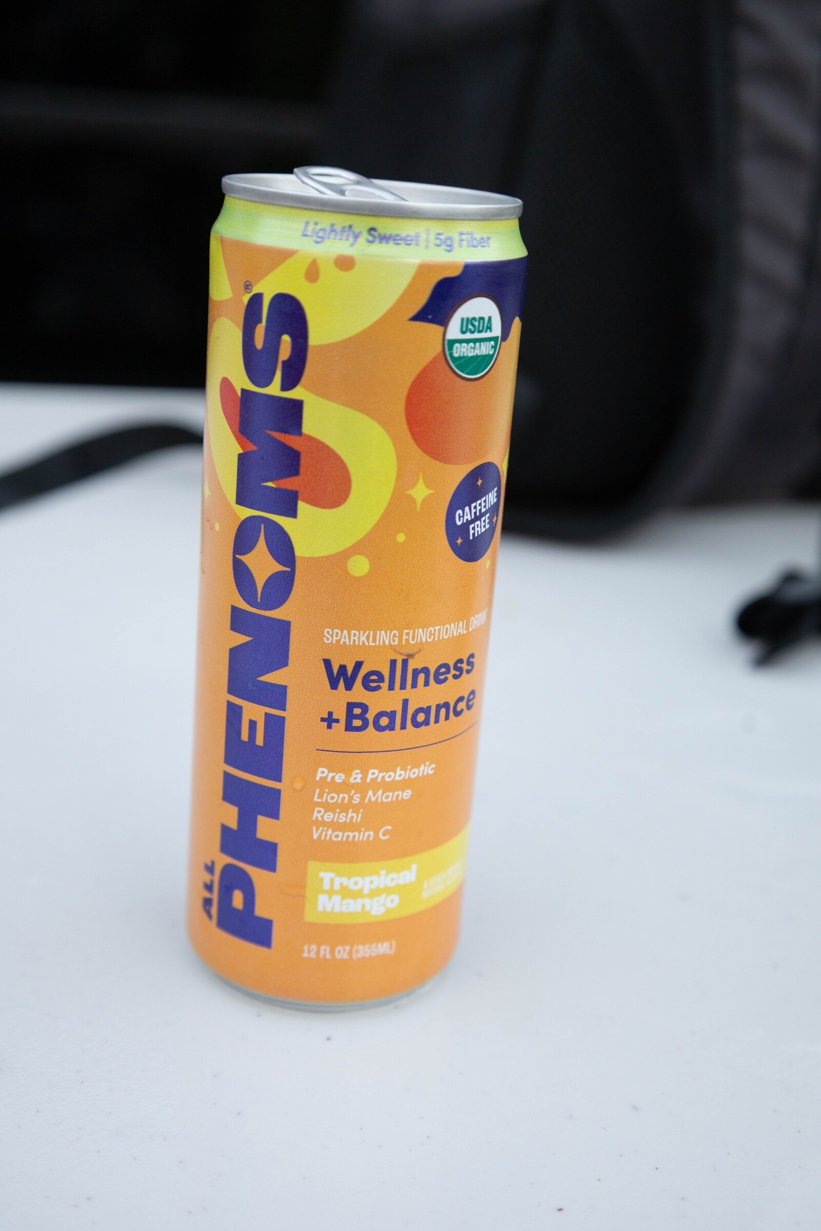An orange and yellow can of Phenoms Wellness + Balance Tropical Mango on a white table.