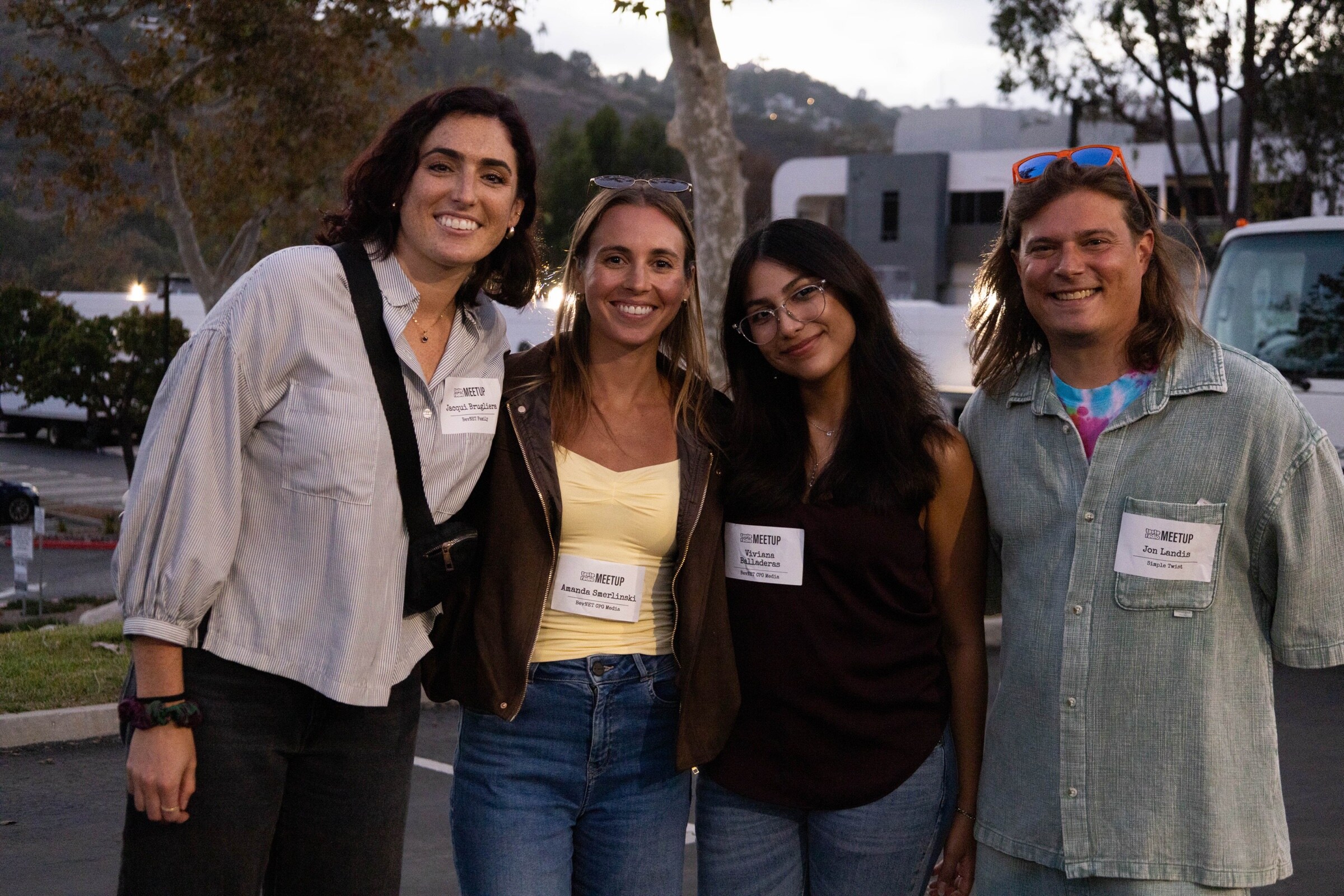 Four smiling people in name badges pose together at dusk in front of trees and hills.