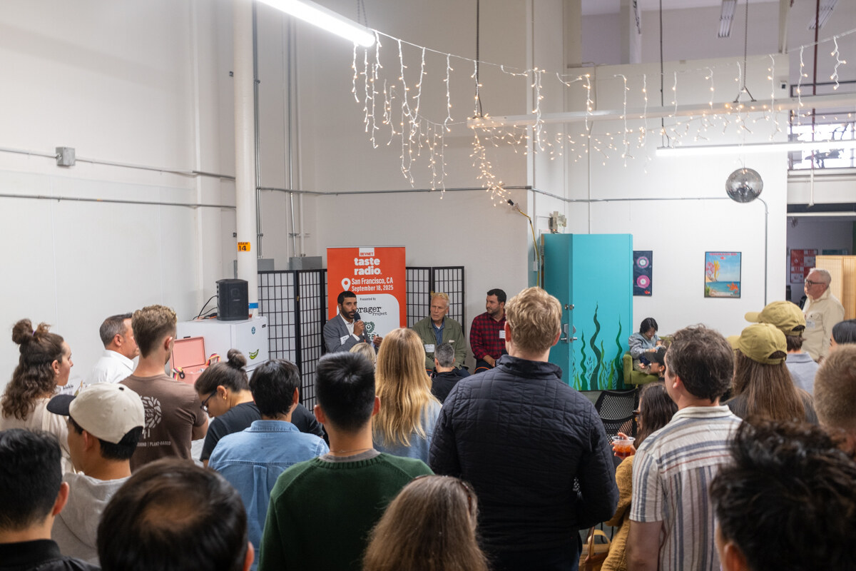 Crowd seen from behind watching a panel in front of the orange Taste Radio banner.
