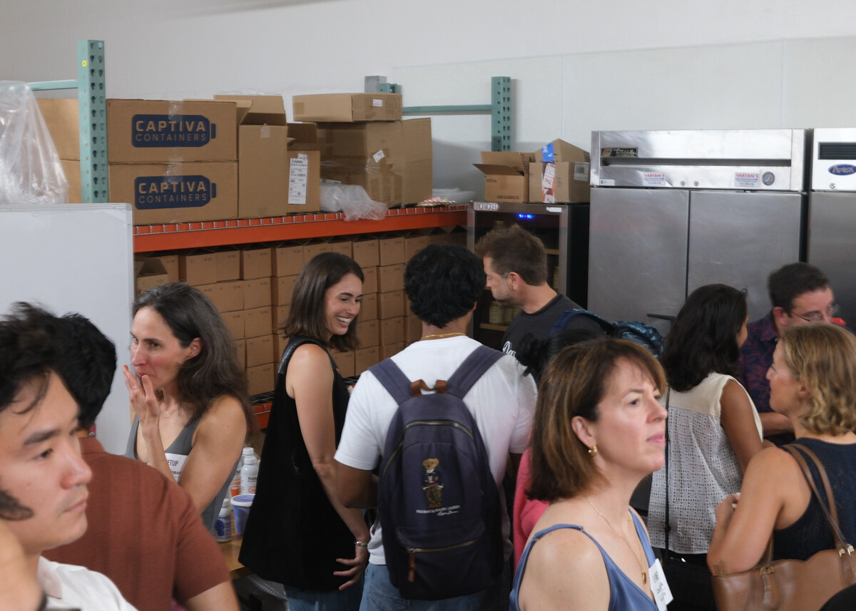 Group of attendees chatting and smiling in front of shelving stacked with boxes.