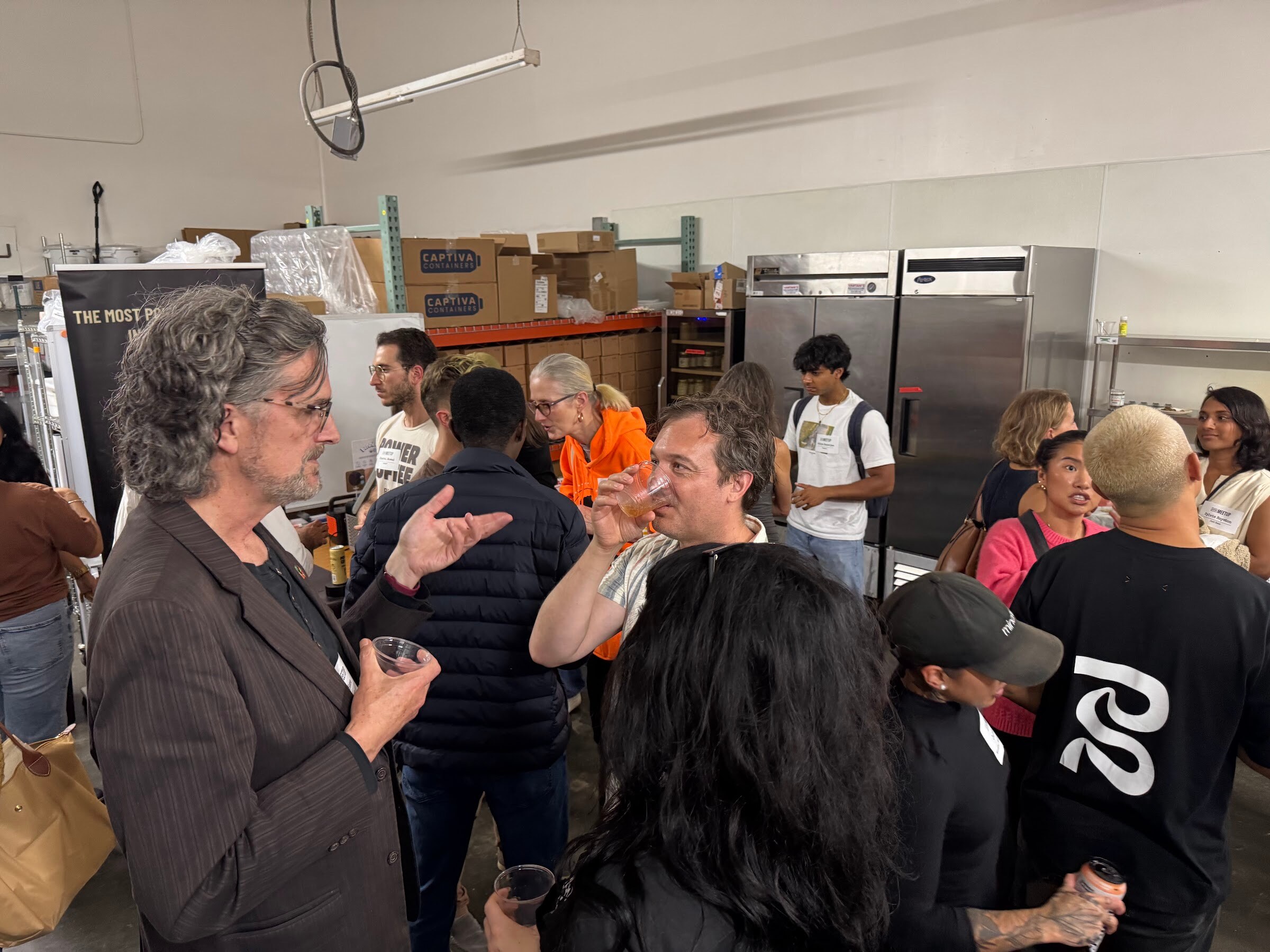 Group of attendees chatting in front of shelving in the warehouse space.