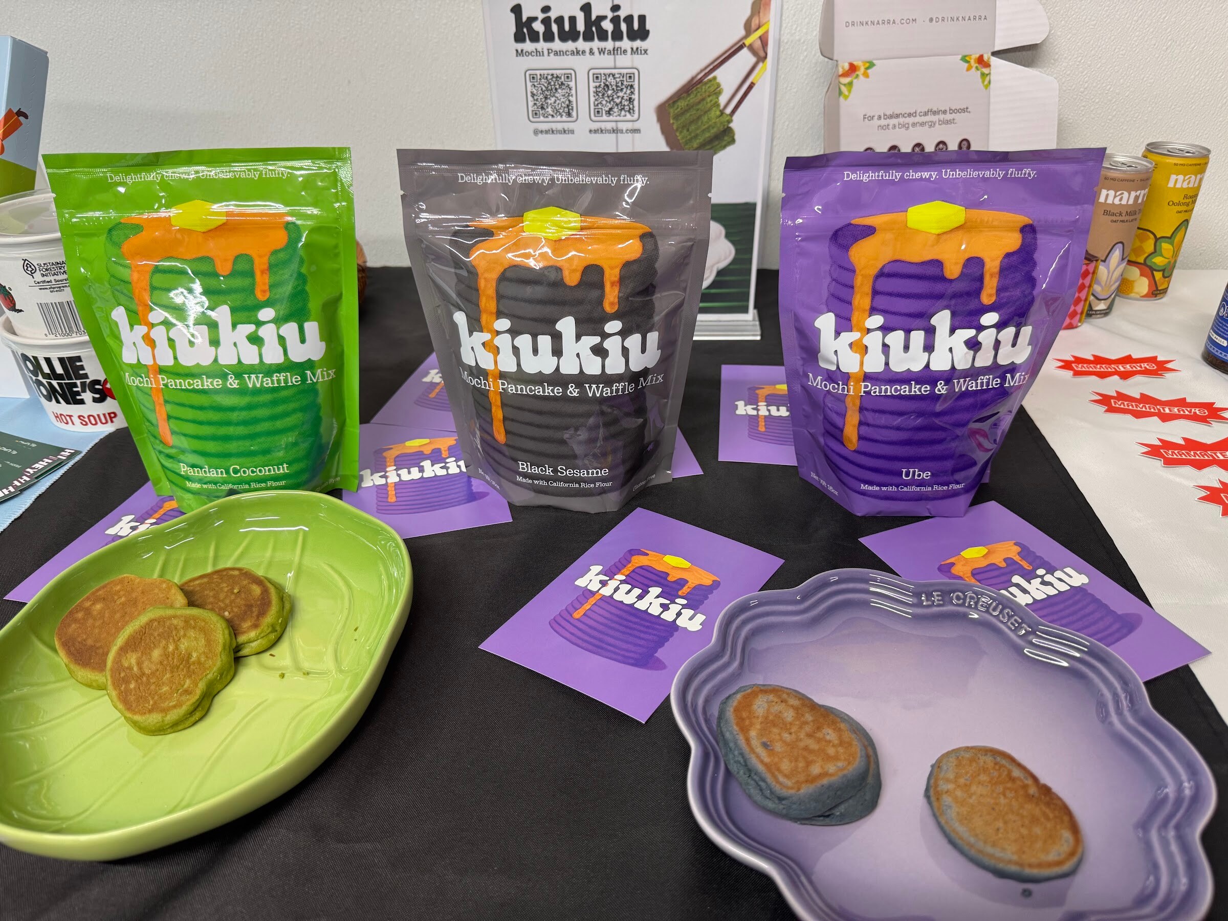 Three bags of kiukiu pancake mix beside plates of pancakes.