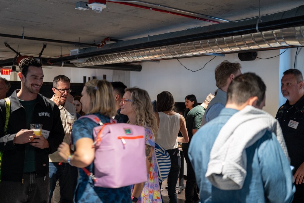 Attendees talking in a crowded room under exposed ductwork.