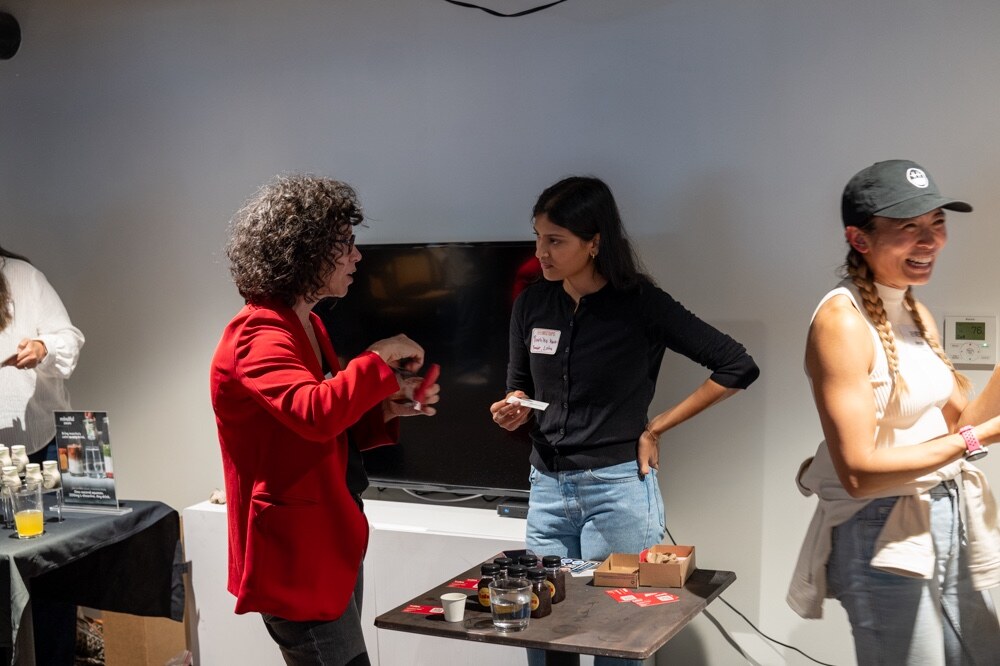 Three women talk and laugh near a small table of samples.