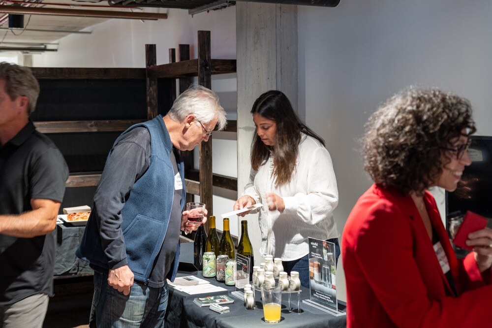 Attendees at a table with wine bottles, cans and glasses of orange juice.