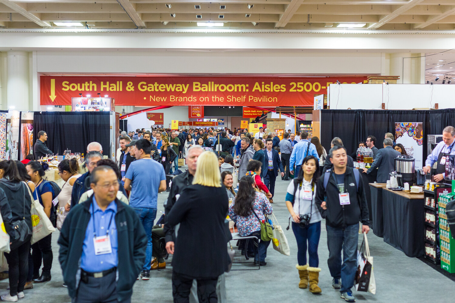 A crowded aisle with a red banner reading South Hall and Gateway Ballroom Aisles 2500 and New Brands on the Shelf Pavilion, with booths on both sides.