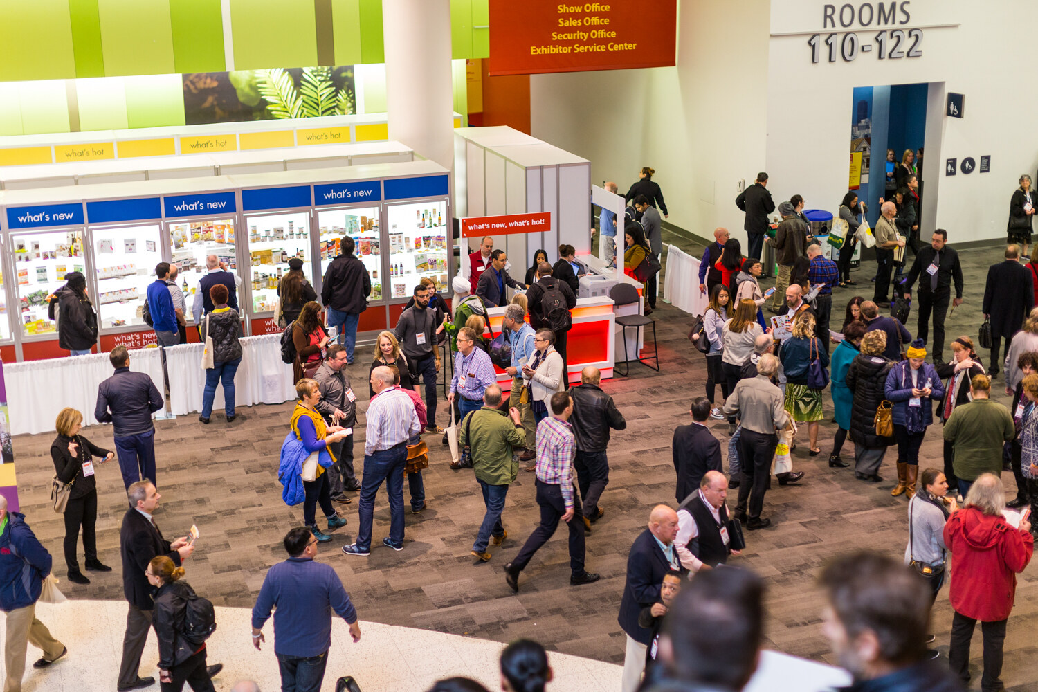 A high-angle view of people standing and walking on a carpeted lobby floor near display cases labeled what's new and a Show Office sign.