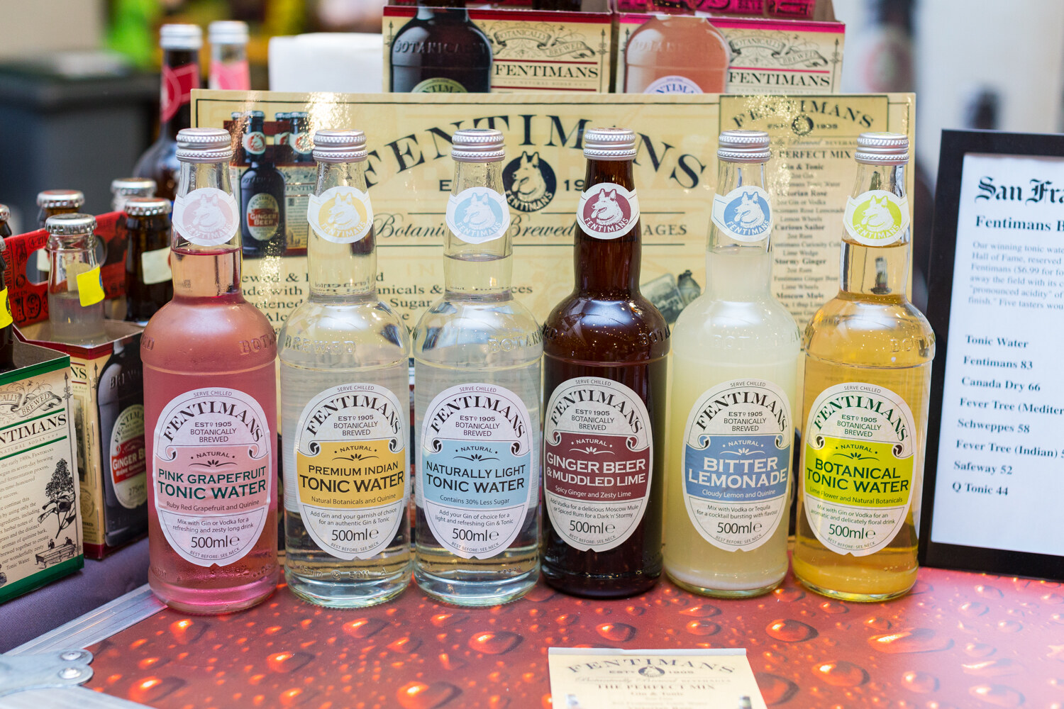 Six bottles of Fentimans including Pink Grapefruit Tonic Water, Premium Indian Tonic Water, Ginger Beer and Muddled Lime, Bitter Lemonade and Botanical Tonic Water in front of a Fentimans display.