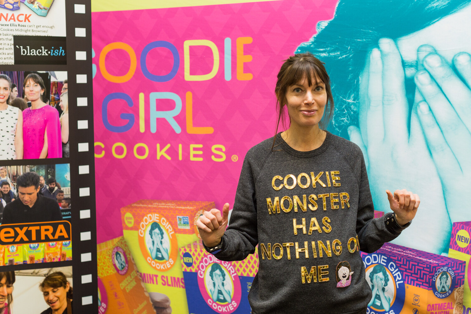 A woman in a gray sweatshirt reading Cookie Monster Has Nothing on Me points both thumbs sideways in front of a pink Goodie Girl Cookies backdrop.