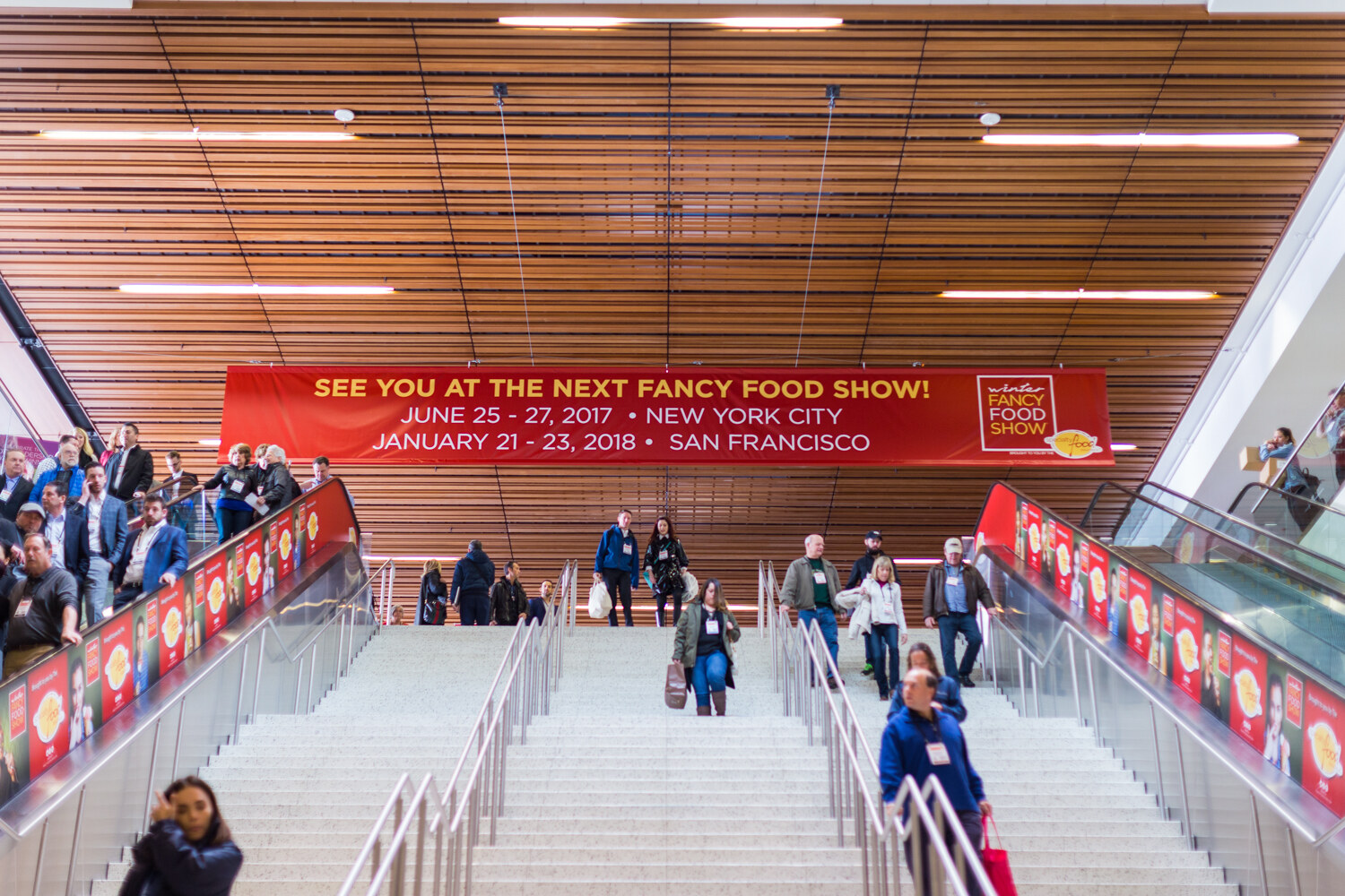 A wide staircase with escalators on both sides under a red banner reading See you at the next Fancy Food Show, June 25-27 2017 New York City, January 21-23 2018 San Francisco.