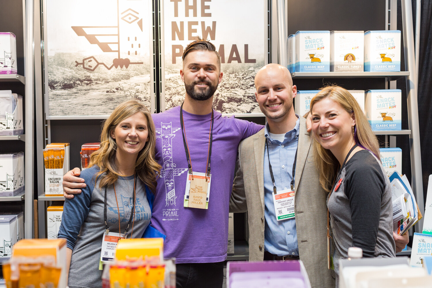 Two women and two men pose in front of shelves of The New Primal jerky packs and Snack Mates Kids boxes.