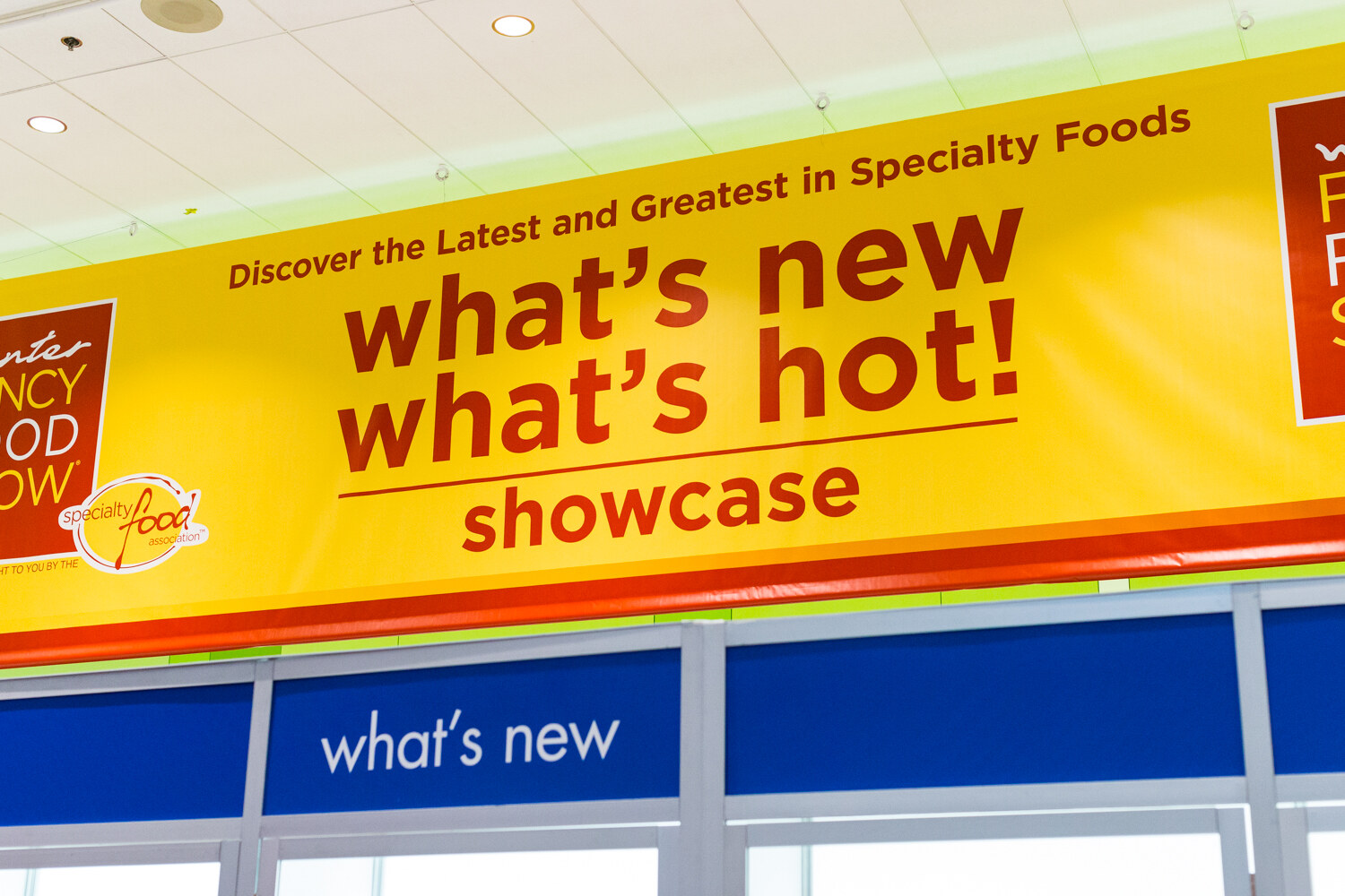 A large yellow banner reading Discover the Latest and Greatest in Specialty Foods, what's new what's hot showcase, above blue what's new signs.