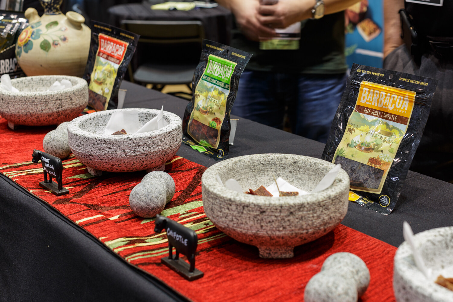 Stone sample bowls on a red runner with bags of jerky behind them.
