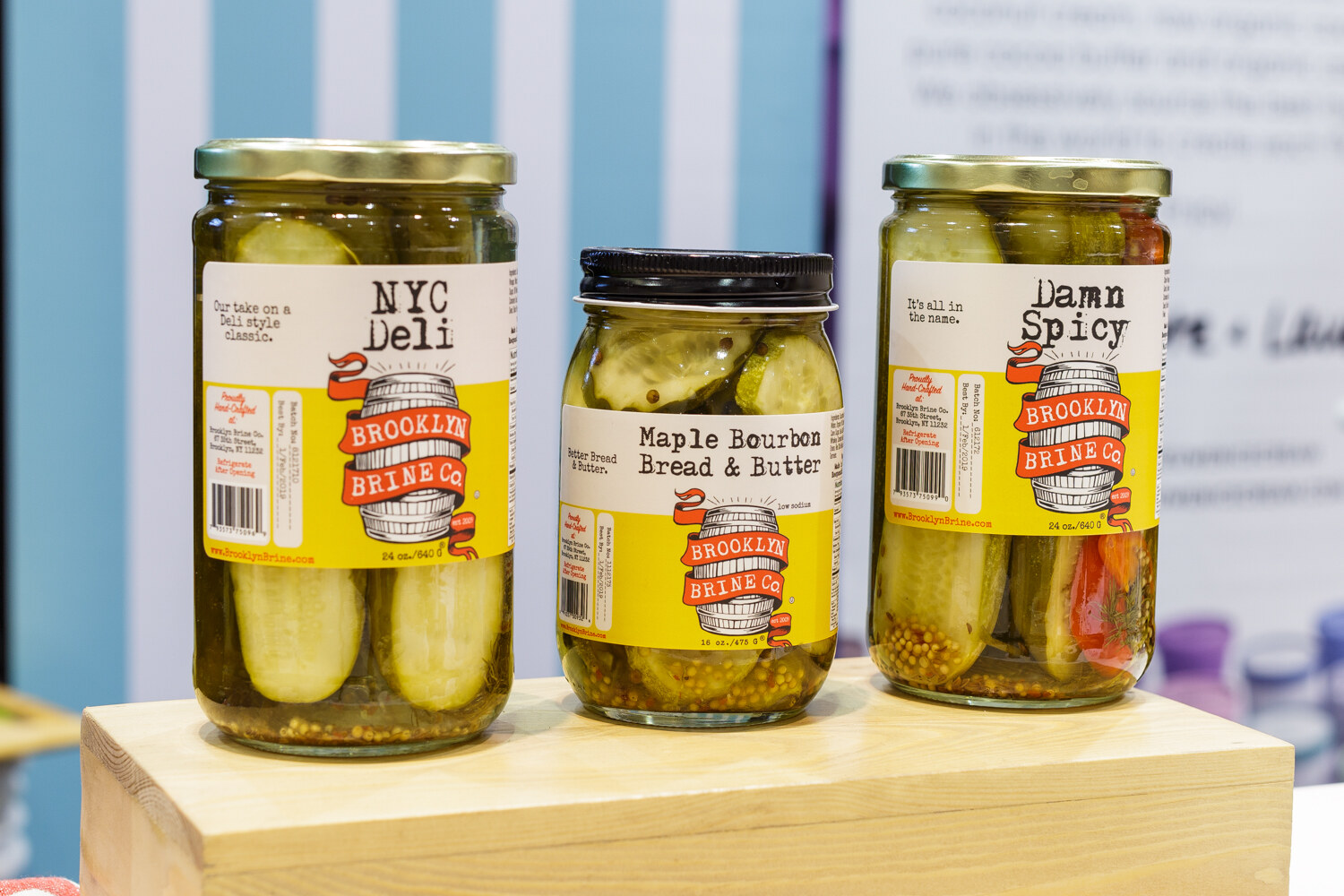 Three jars of pickles on a wood riser.