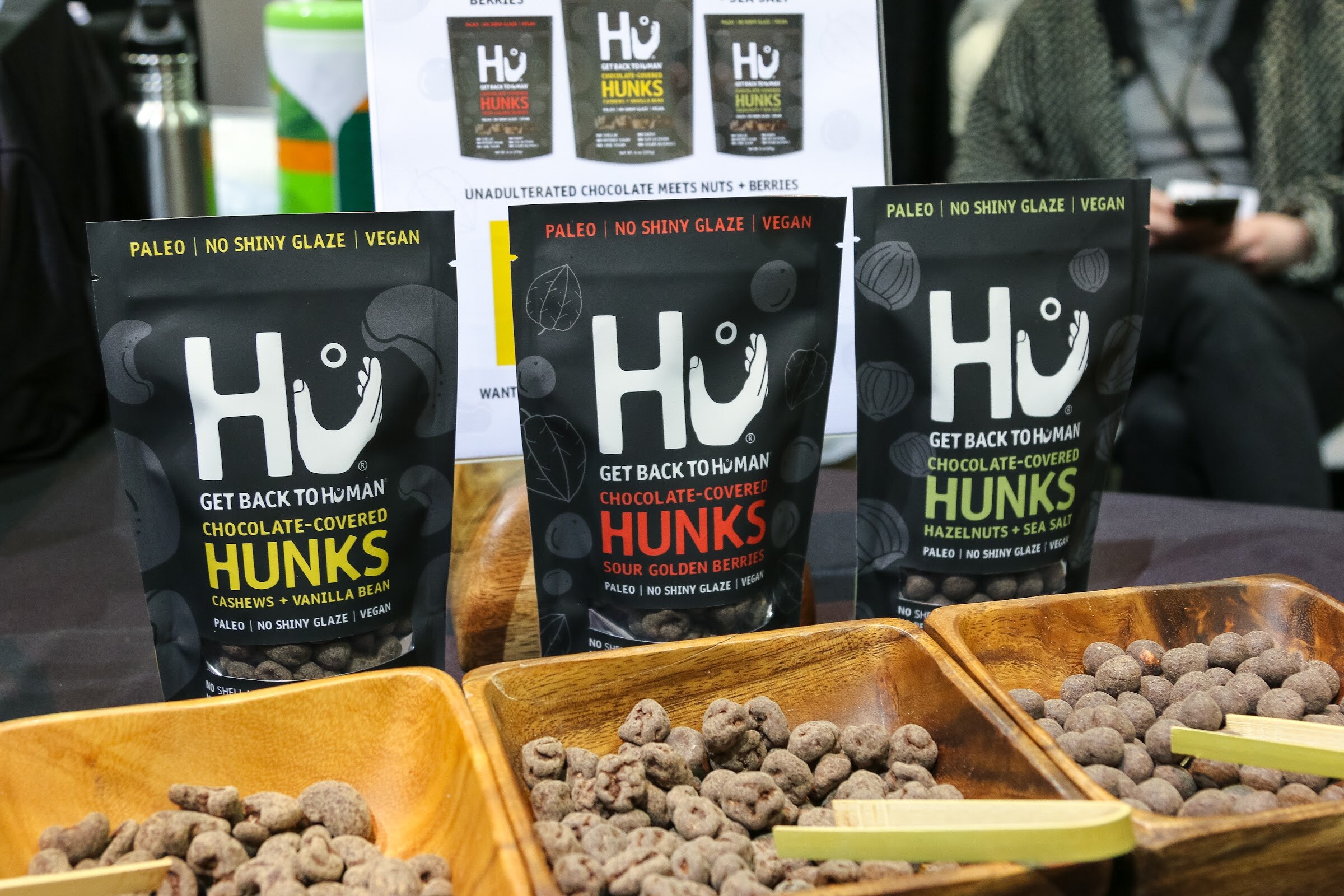 Bags of Hu Hunks behind bowls of chocolate-covered nuts.