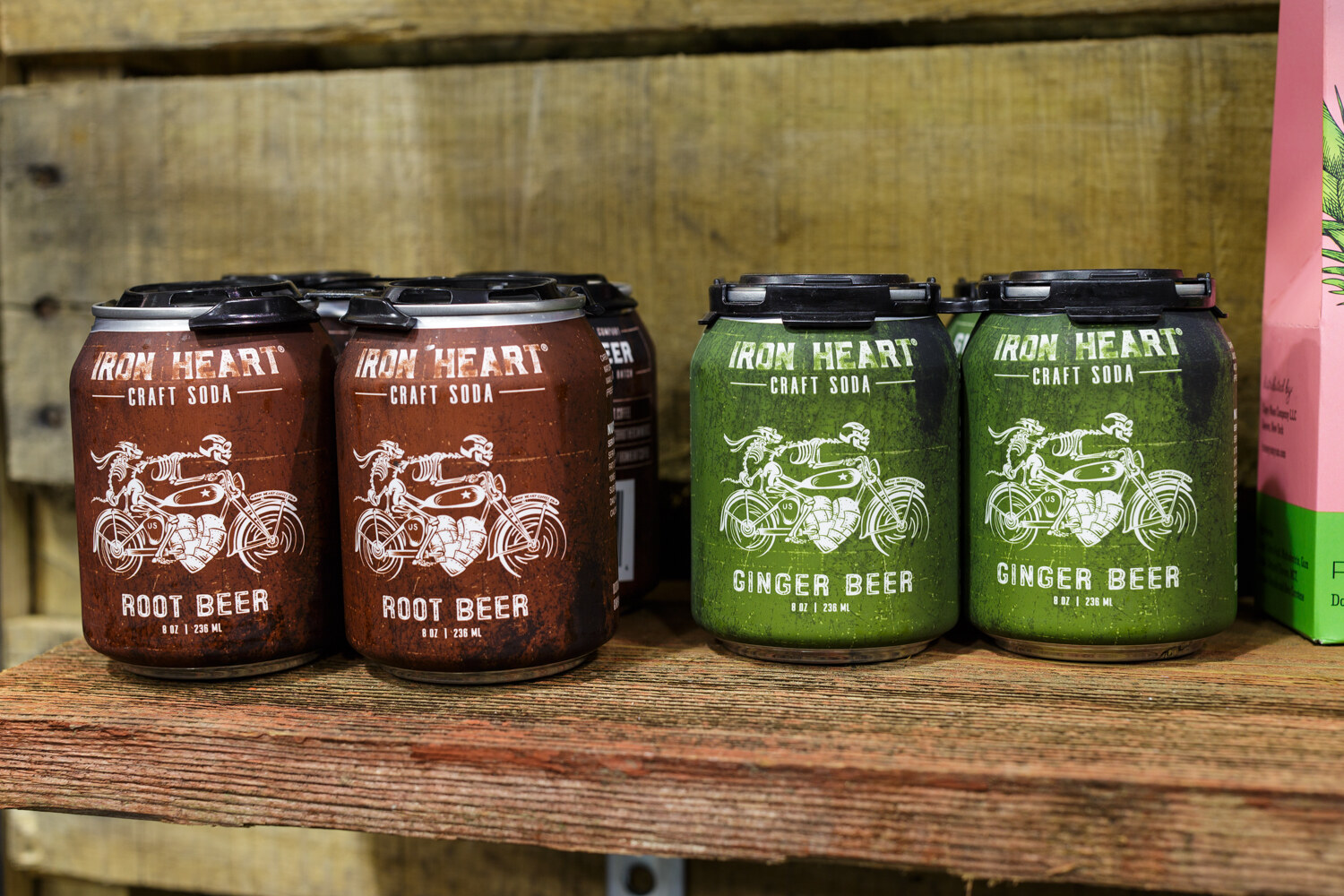Small cans of Iron Heart craft soda on a rustic wooden shelf.