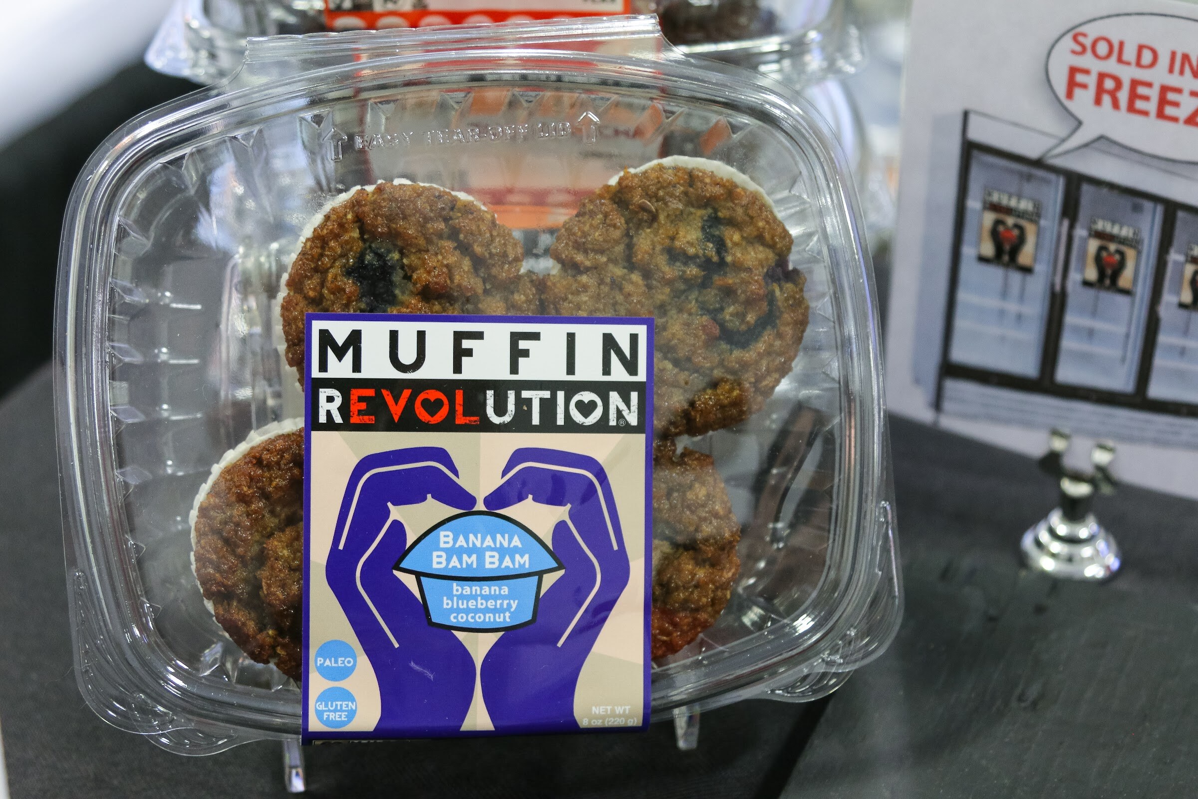 A clear container of banana blueberry coconut muffins with a Muffin Revolution label.