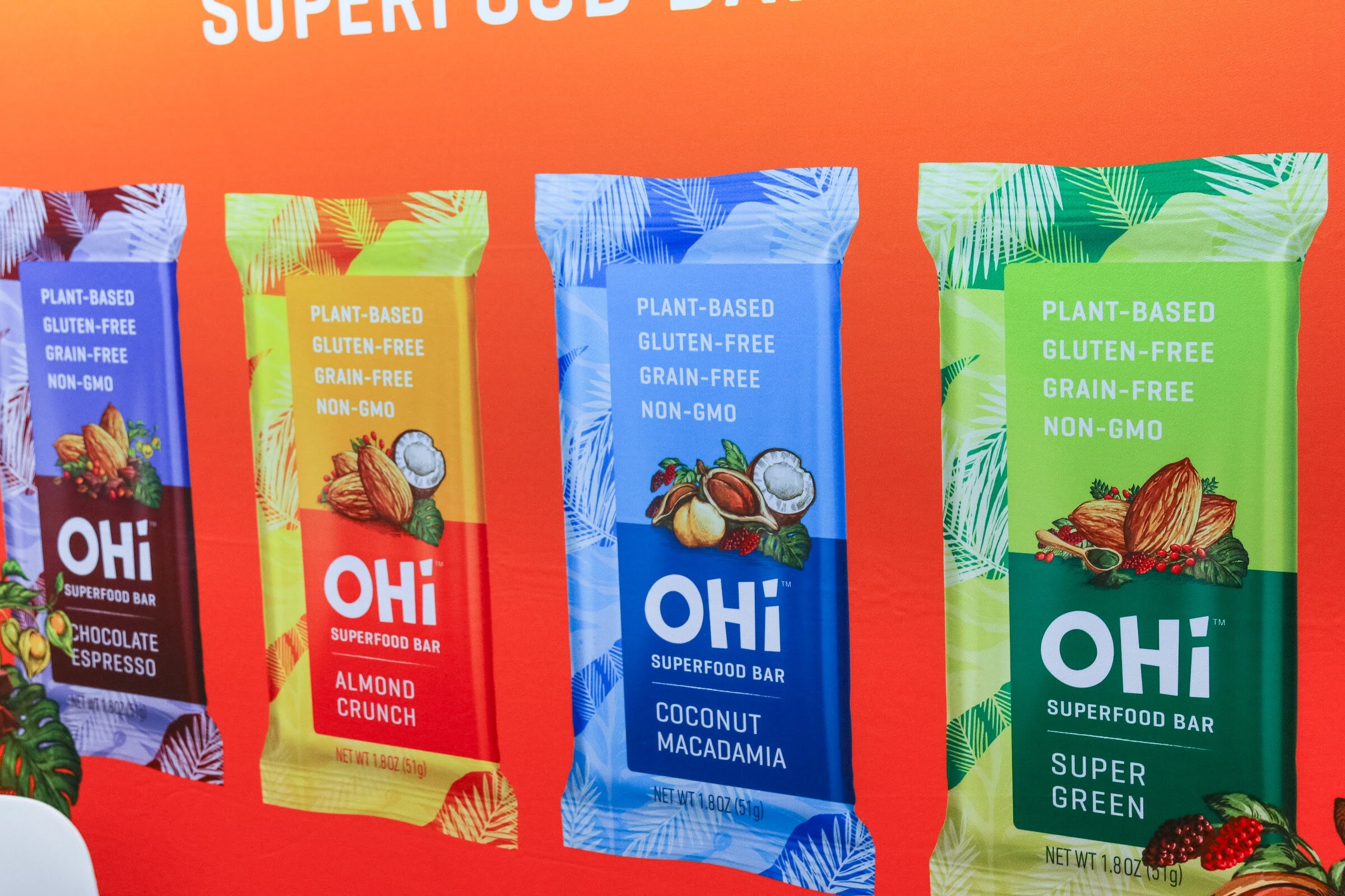 Four OHi superfood bars in different flavors against an orange background.