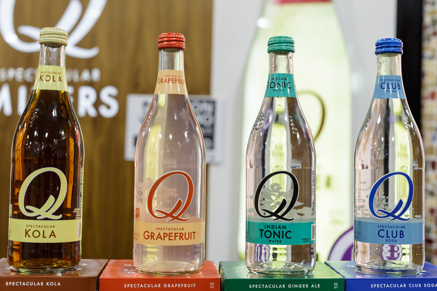Glass bottles of mixers in front of a Q Mixers sign.
