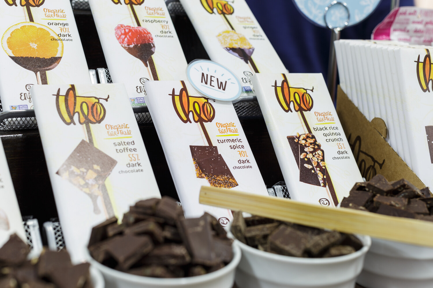 Upright chocolate bars labeled Theo beside white bowls of chocolate pieces.