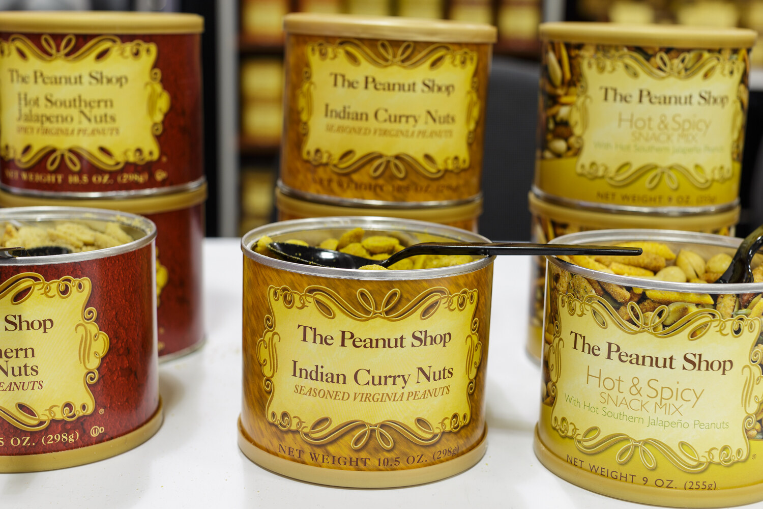 Tins of seasoned nuts with spoons on a table.