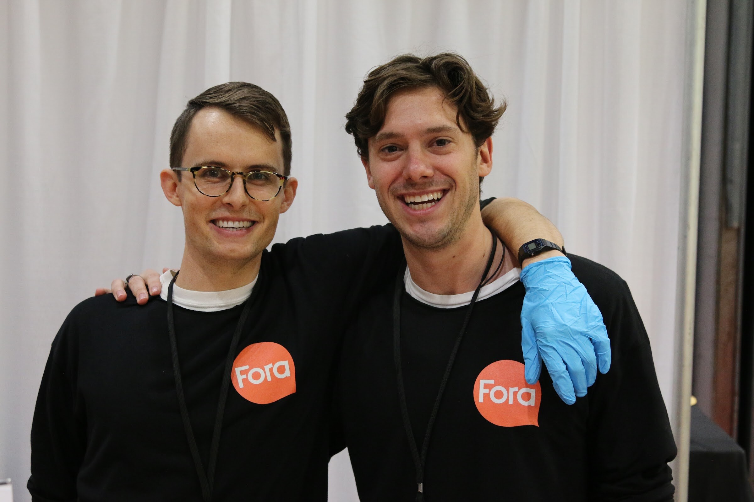 Two men in black Fora shirts smiling with their arms around each other.