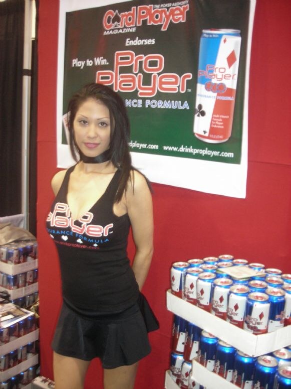 A woman in a black Pro Player tank top and skirt stands before a Card Player Magazine banner, with stacked Pro Player cans on display beside her.