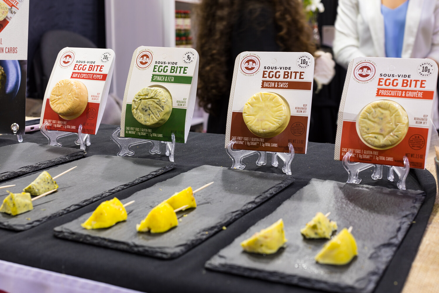 Photo of sous-vide egg bites on slate trays beside four Egg Bite packages.