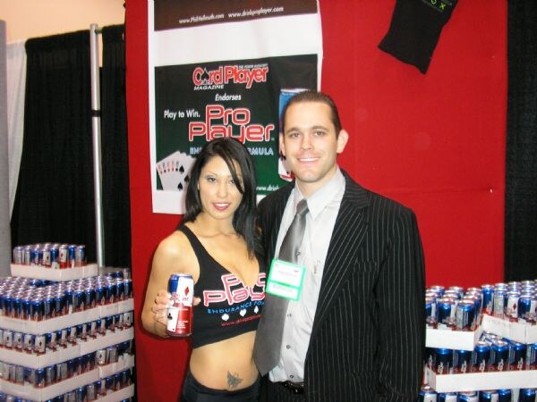 A woman in a Pro Player top holds a can next to a man in a pinstripe suit with a badge, in front of a Card Player Magazine banner and stacked cans.