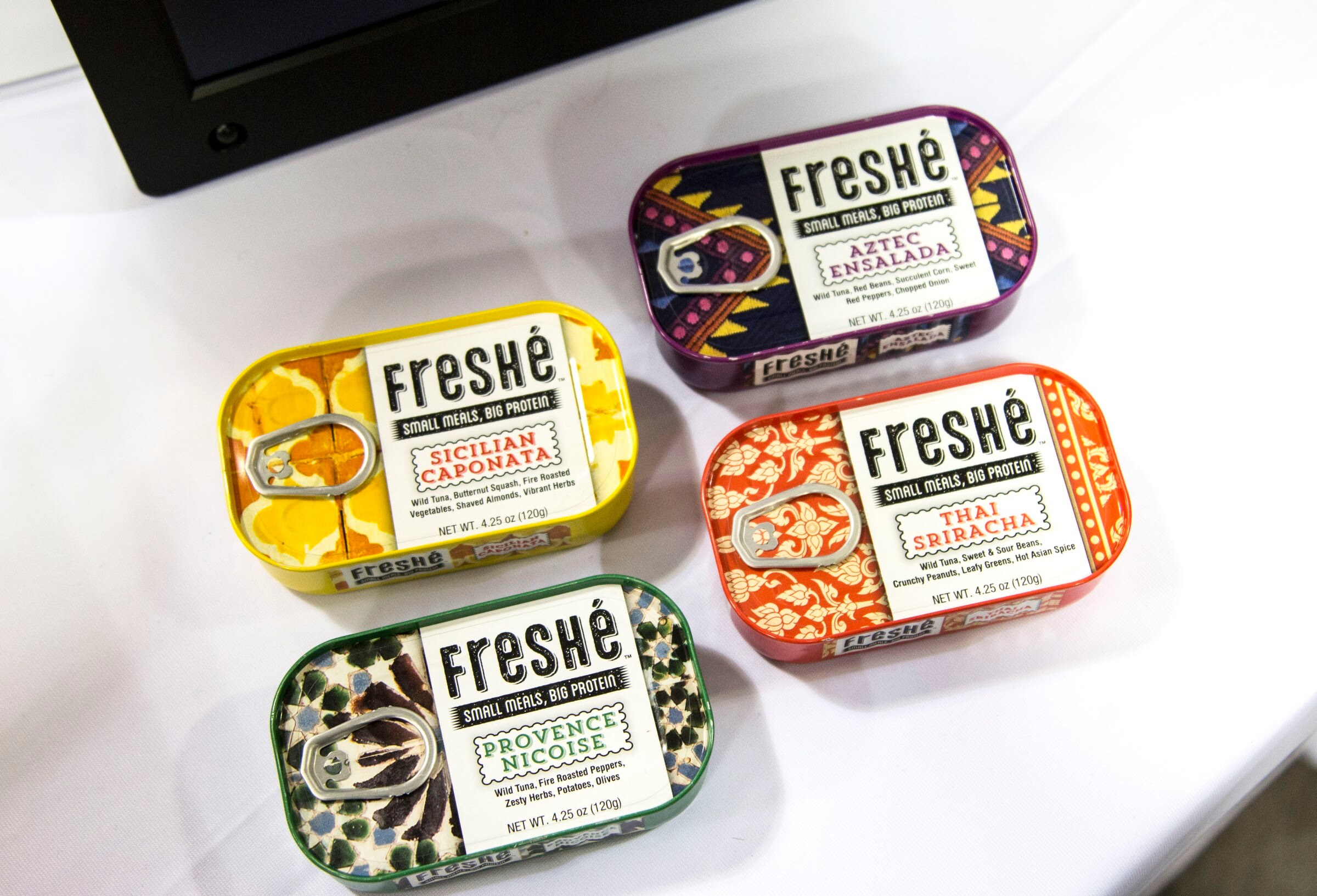 Photo of four decorative Freshe small snacks tins with bold artwork.