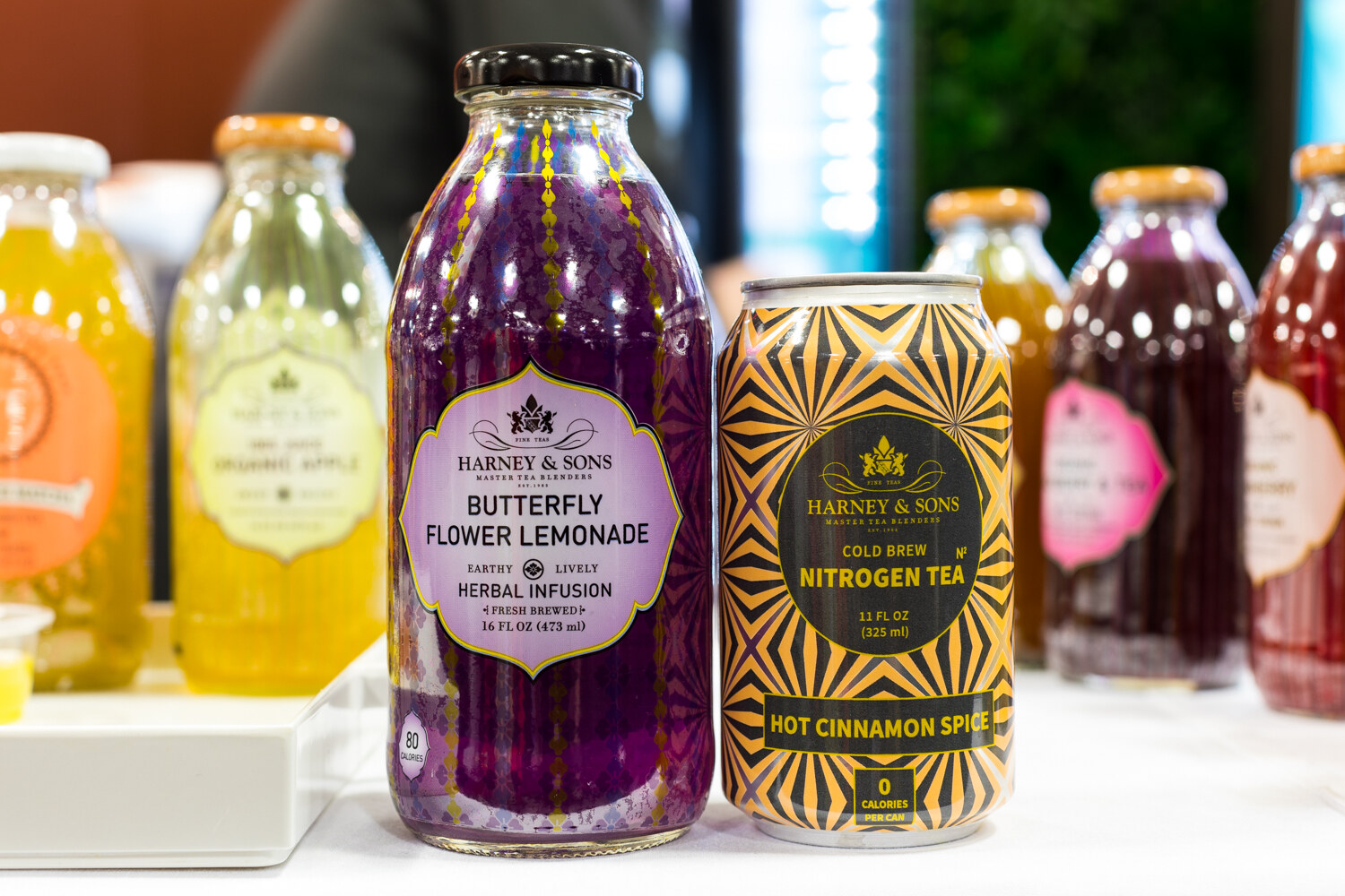 Photo of Harney & Sons butterfly flower lemonade and nitrogen tea bottles beside a row of other bottles.