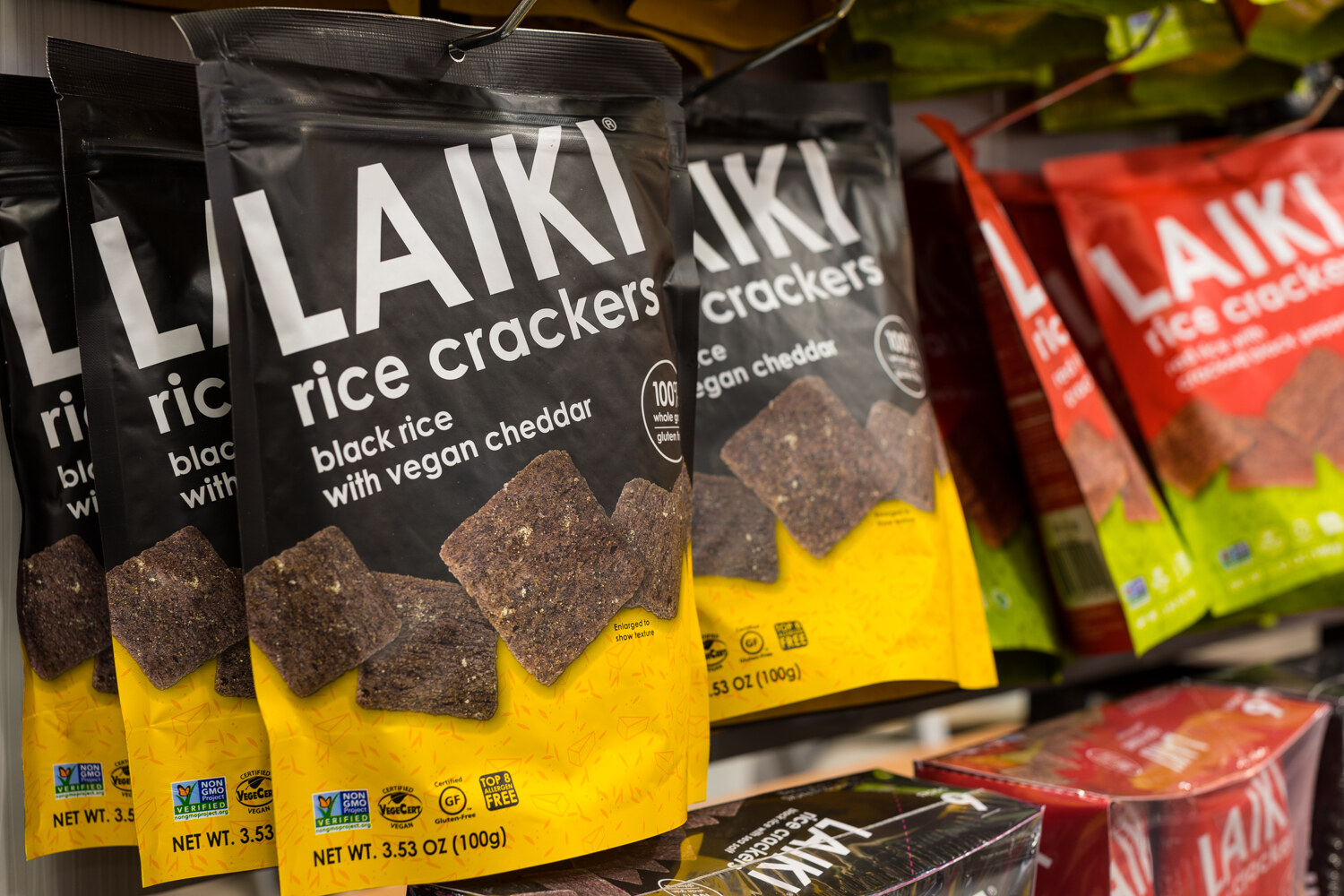 Photo of bags of Laiki rice crackers in black rice and cheddar flavors on a shelf.