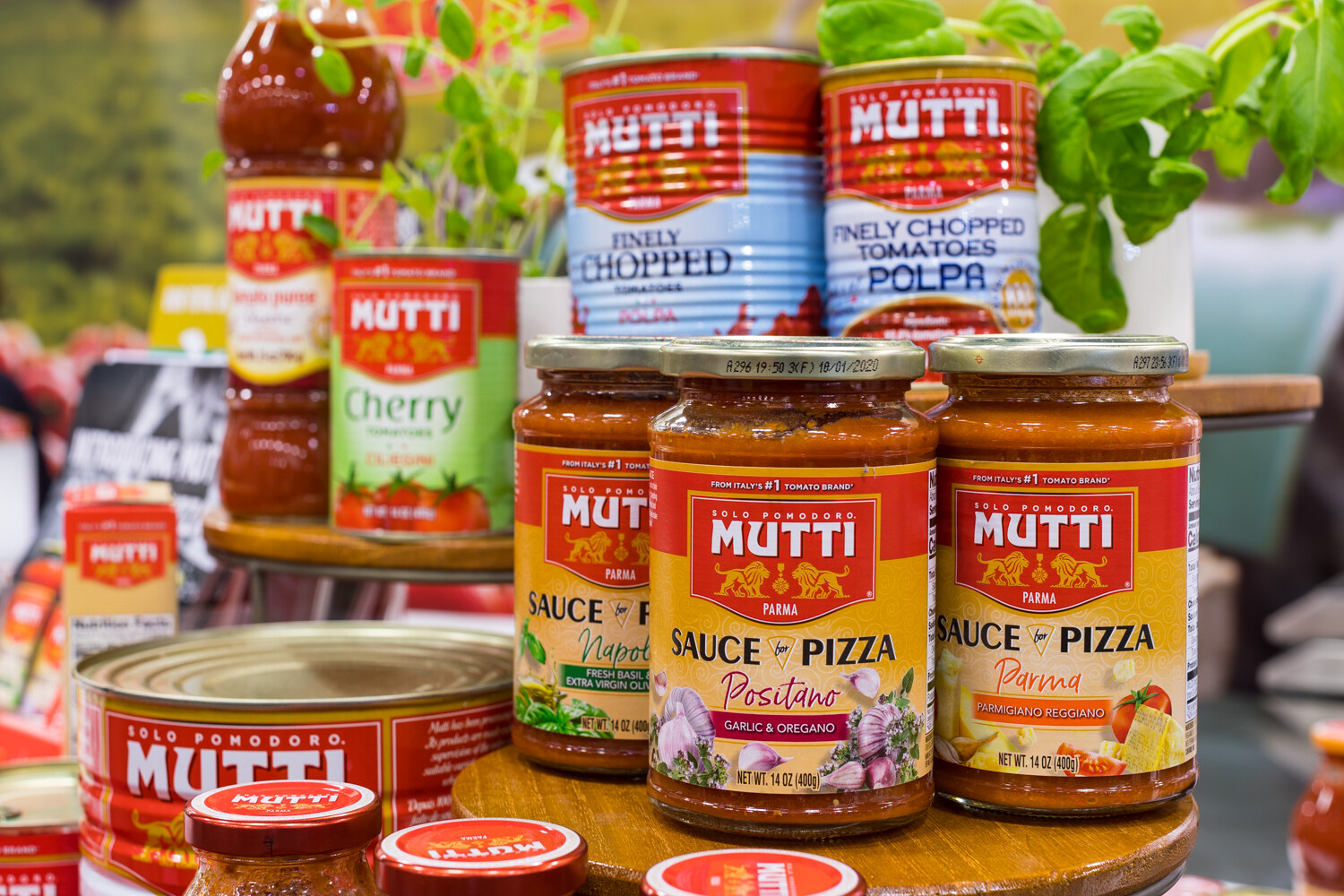 Photo of jars and cans of Mutti tomatoes and pizza sauces with fresh basil.