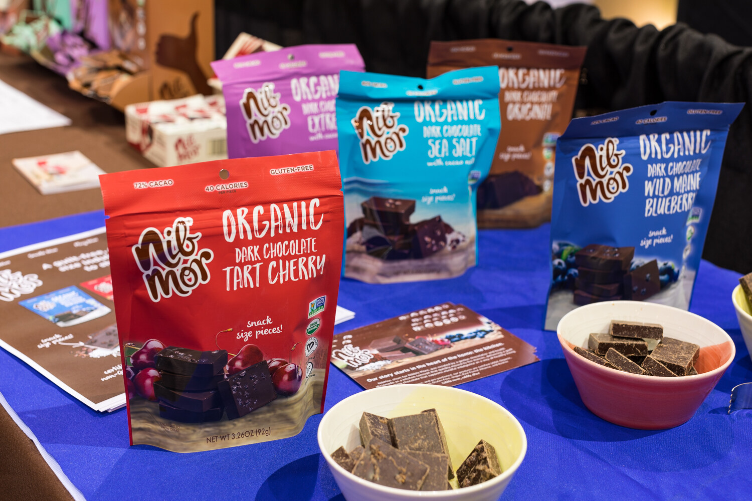 Photo of Nib Mor organic dark chocolate snack bags and tasting bowls on a blue tablecloth.