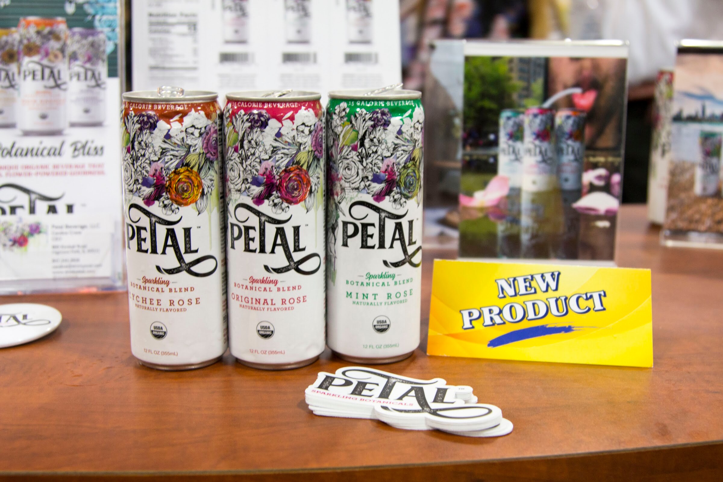 Photo of three cans of Petal sparkling botanical rose beverage with a New Product card.