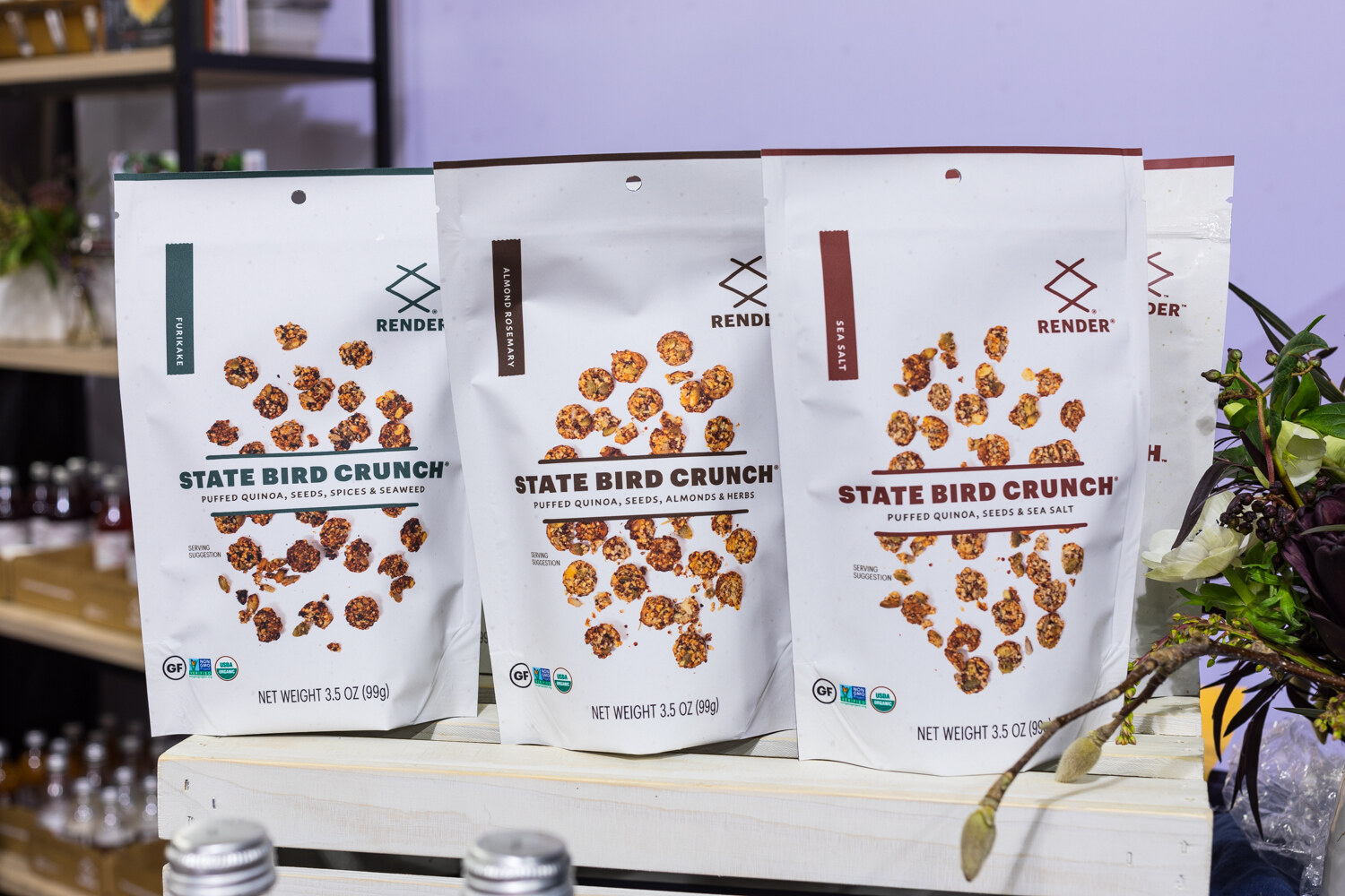 Photo of bags of Render State Bird Crunch beside floral decor.