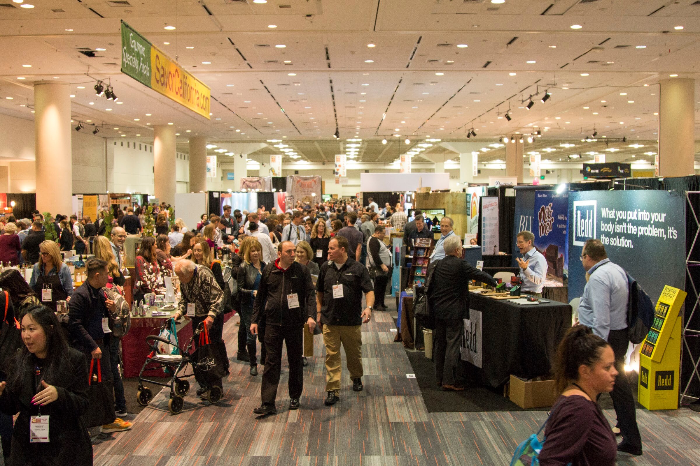 Photo of a crowded exhibit hall with attendees walking between booths.