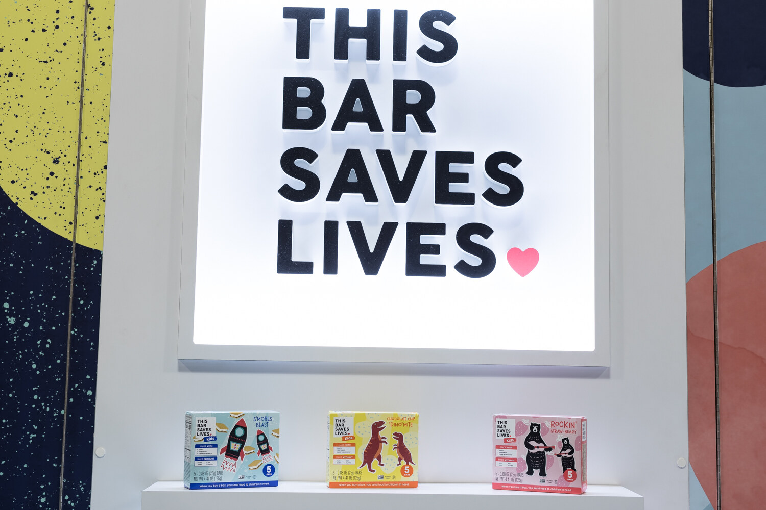 Photo of a lit THIS BAR SAVES LIVES sign above small bar boxes.