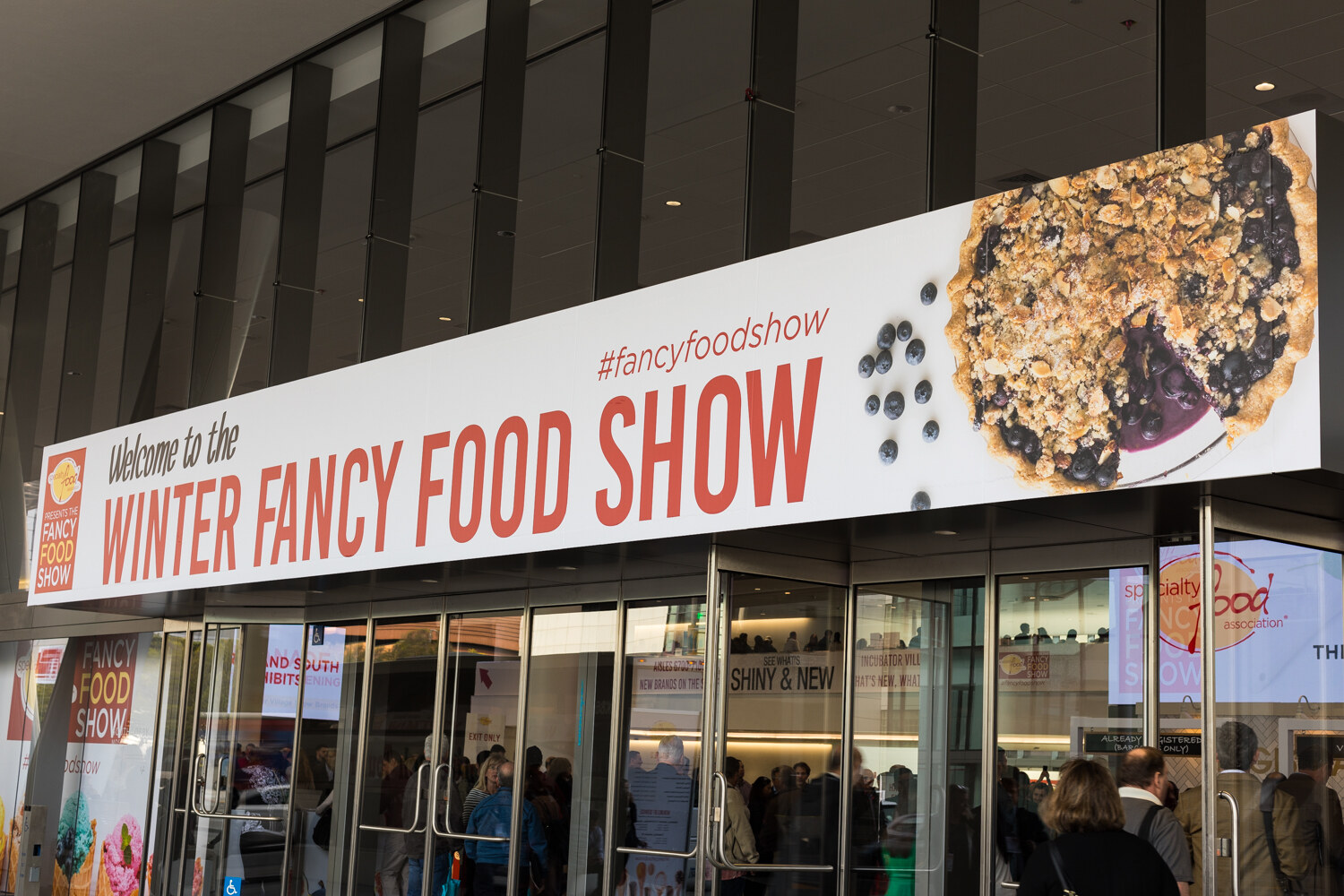 Photo of the entrance banner reading Welcome to the Winter Fancy Food Show with attendees entering.