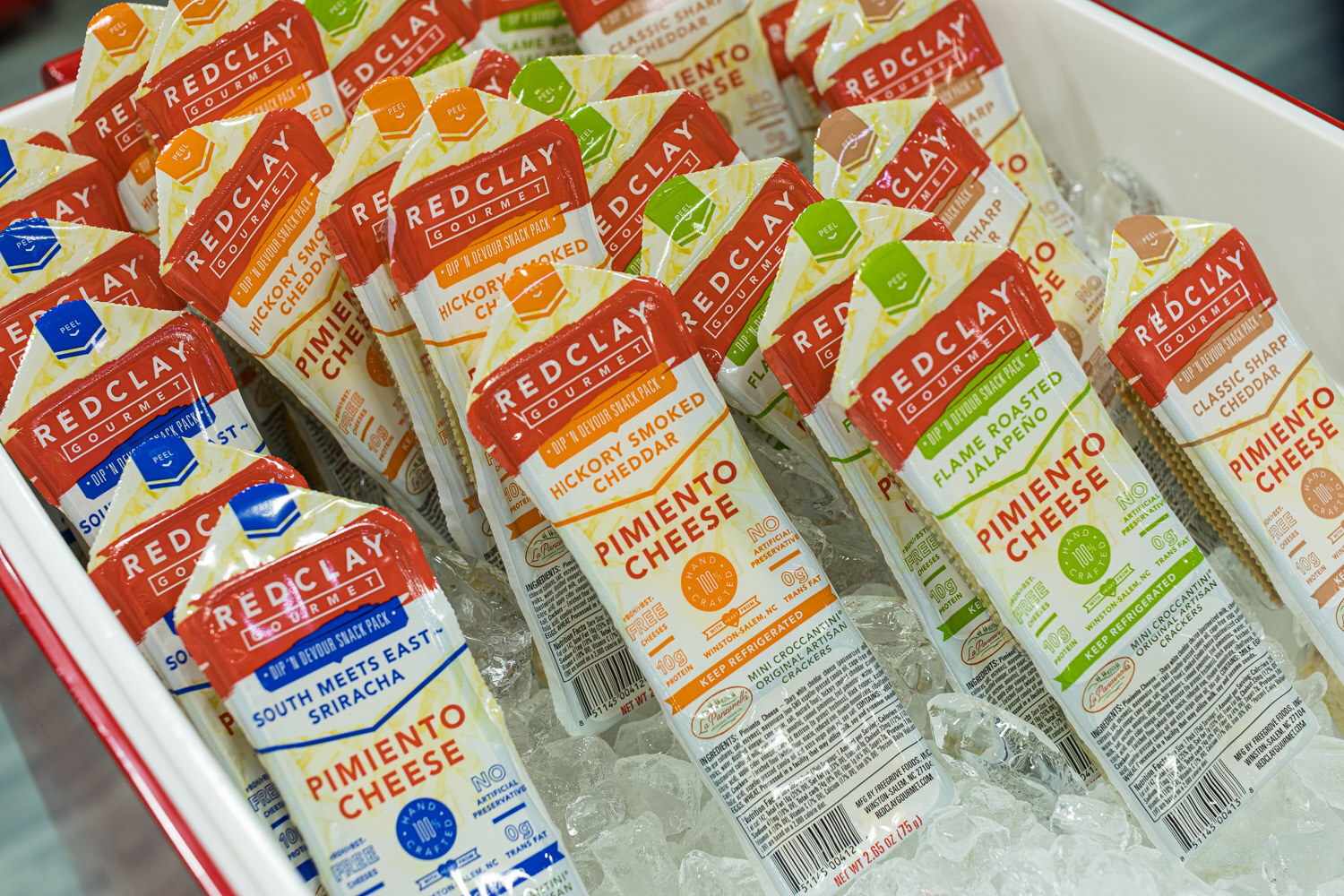 Dozens of RedClay Gourmet pimiento cheese snack packs piled on ice in a red tray