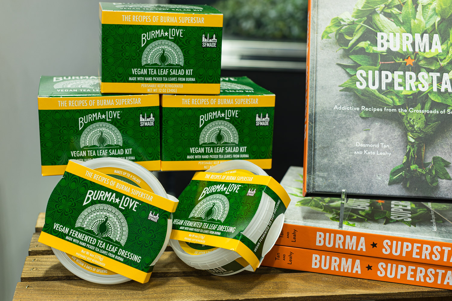 Stacked green Burma Love vegan tea leaf salad kits and dressing tubs next to copies of the Burma Superstar cookbook