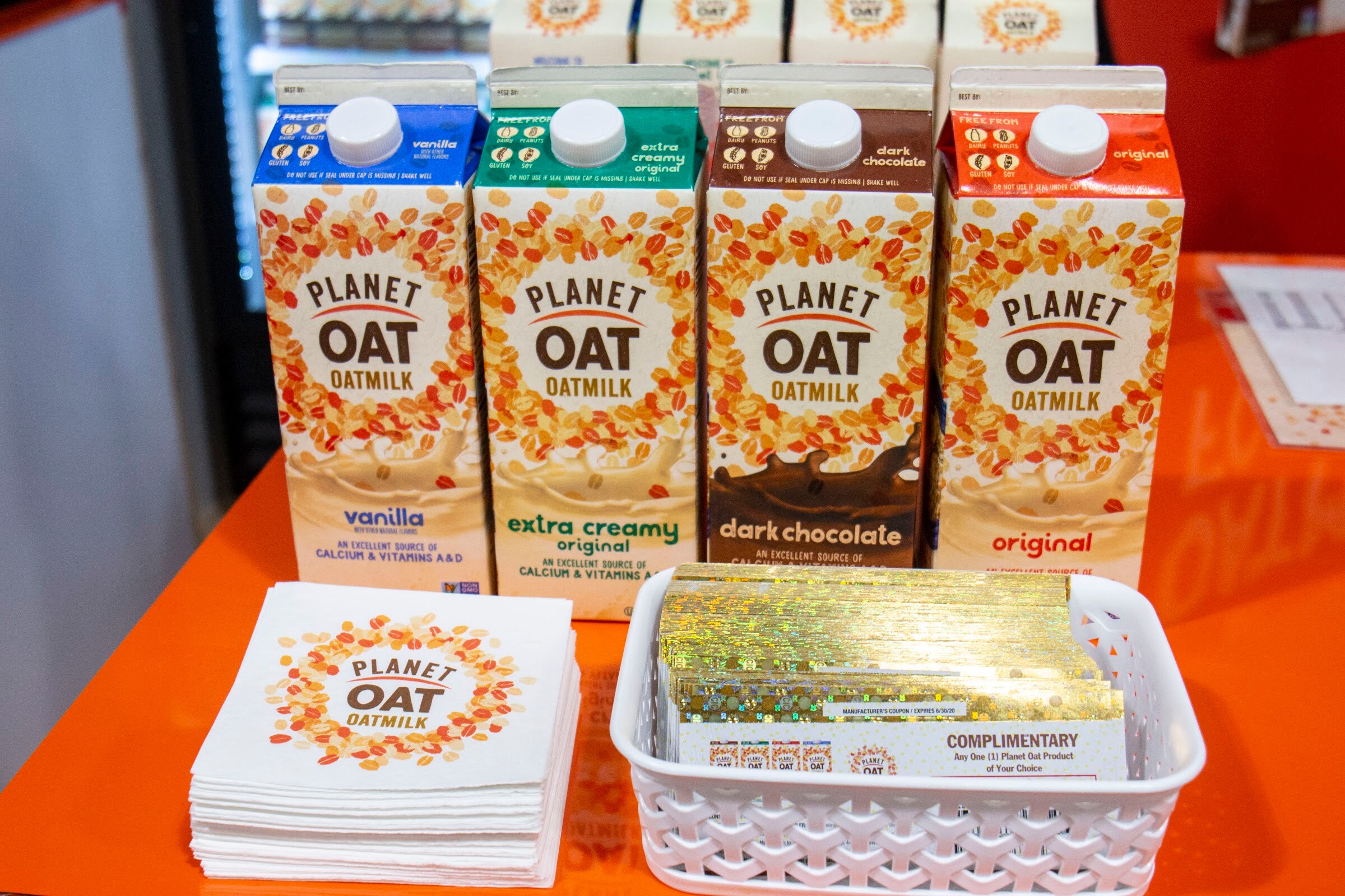 Four Planet Oat cartons in vanilla, extra creamy, dark chocolate and original beside a stack of napkins