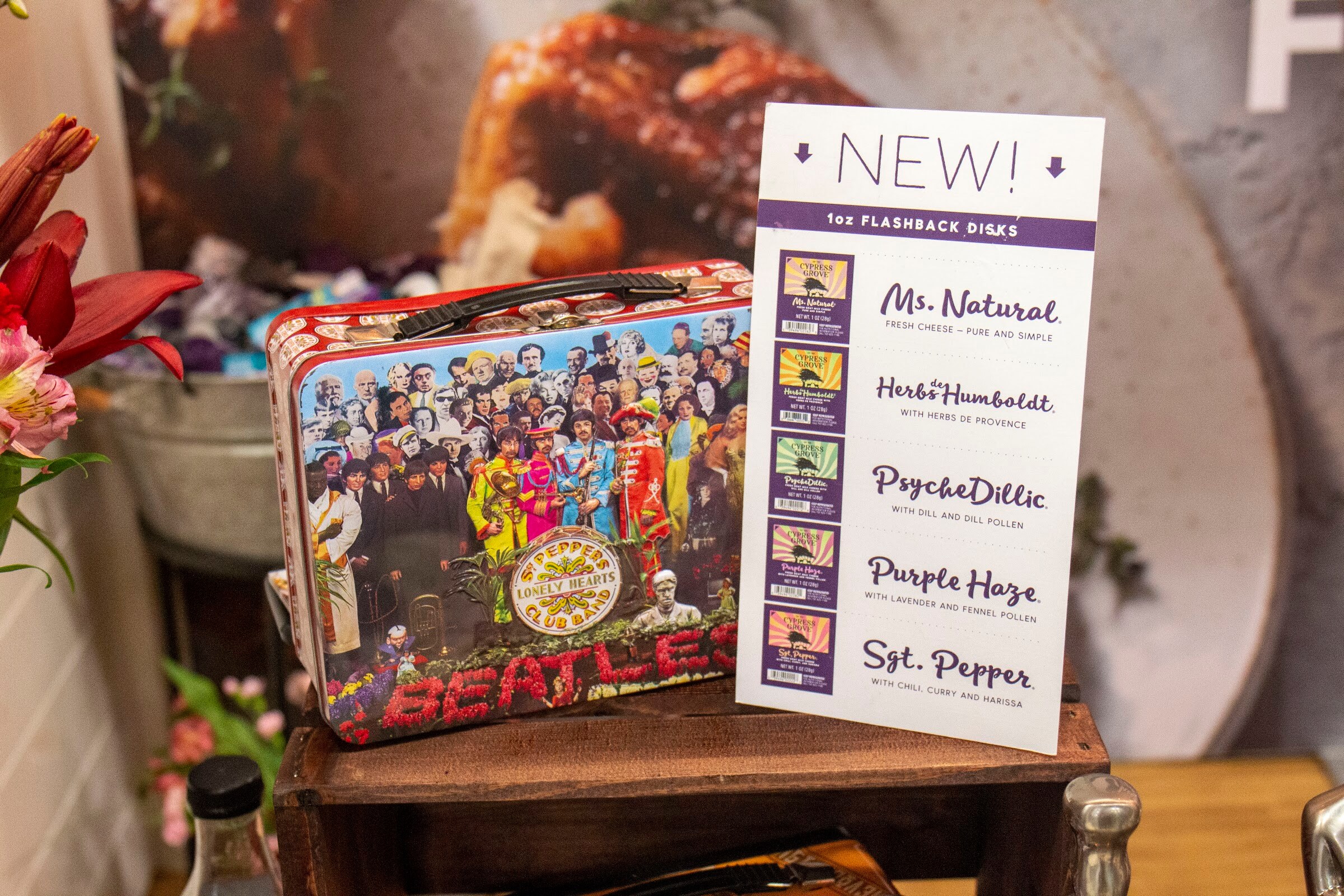 A Sgt. Pepper-themed lunchbox beside a New 1oz Flashback Disks card listing five flavors
