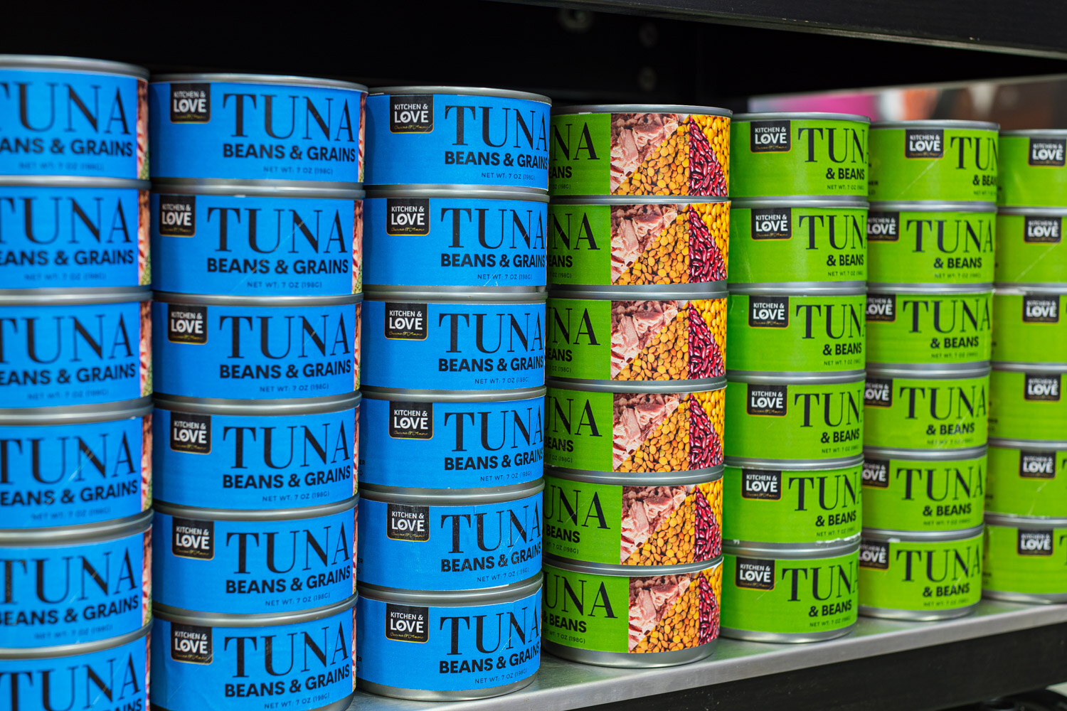 Shelves of blue and green Kitchen and Love cans labeled Tuna Beans and Grains