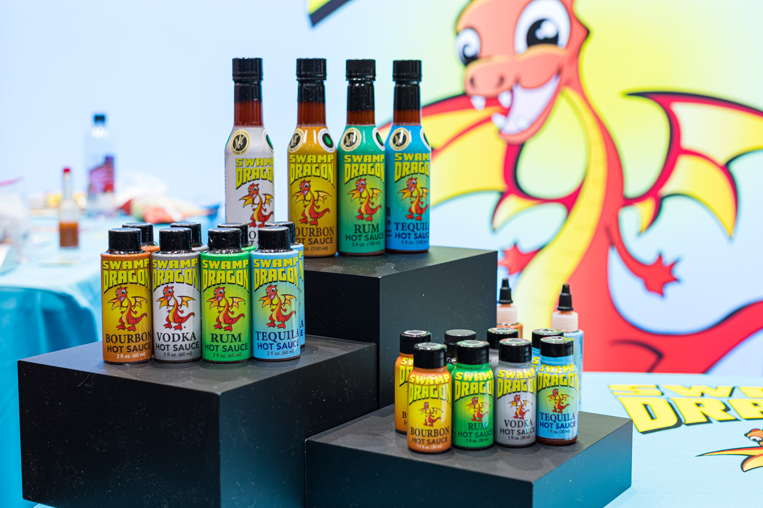 Swamp Dragon hot sauce bottles of several sizes on black display blocks in front of a cartoon dragon