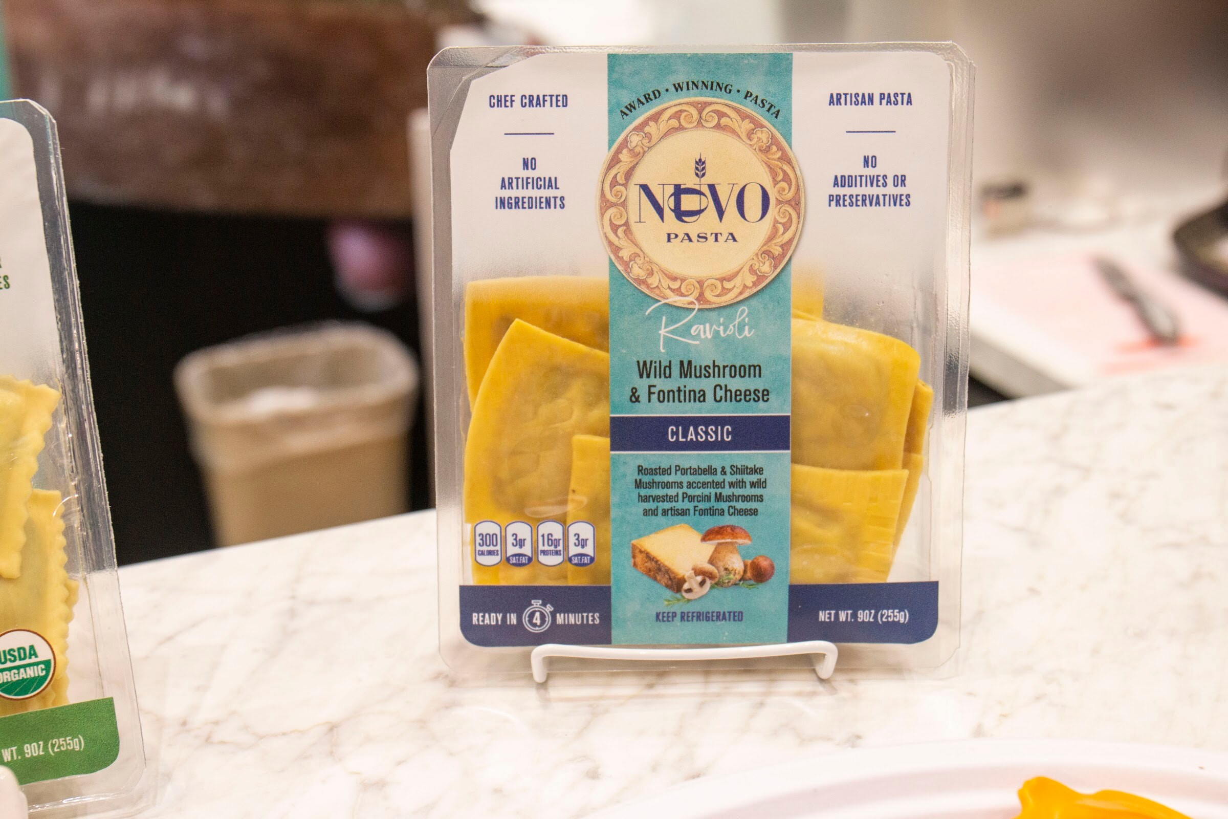 A clear package of Nuovo Pasta ravioli on a small stand on a marble counter