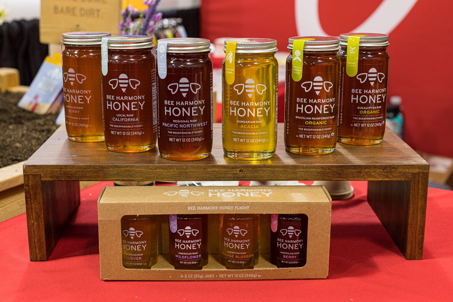 Six jars of Bee Harmony honey on a walnut riser above a boxed honey flight set