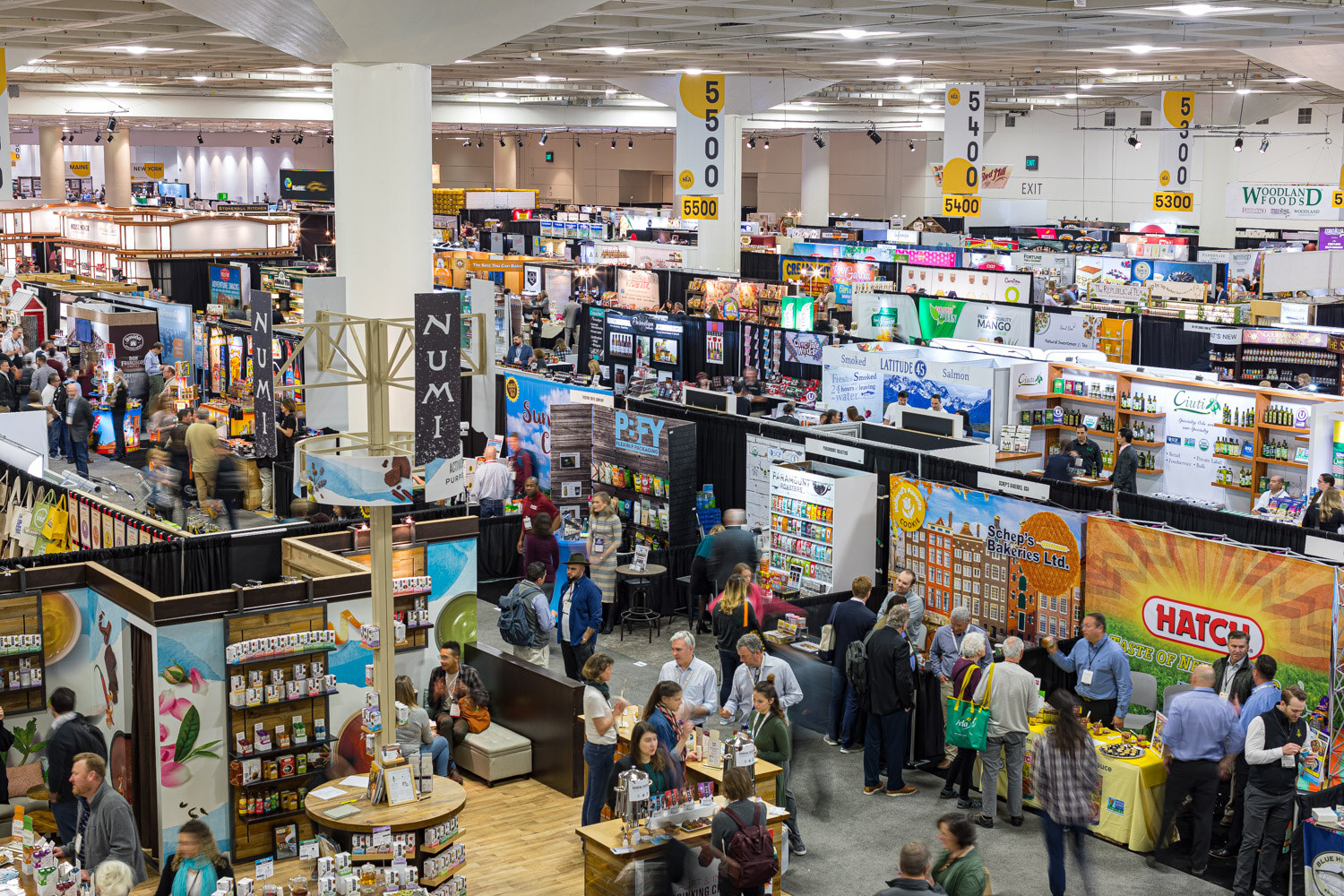 An elevated view of a crowded trade show floor with rows of booths and numbered hanging signs