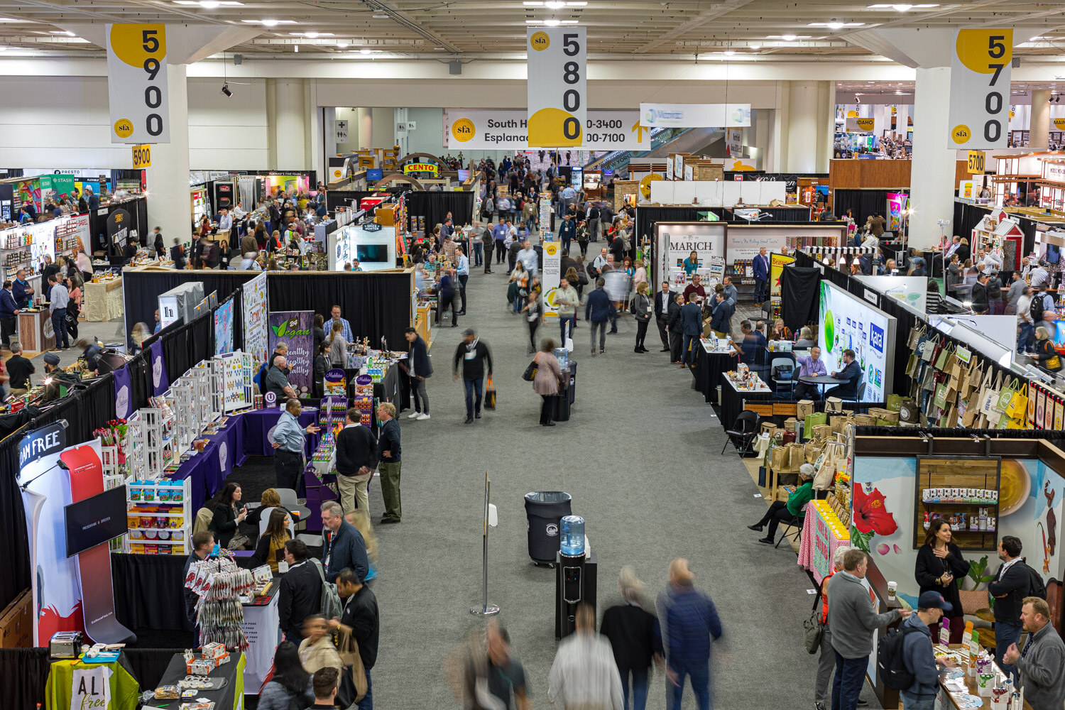 An elevated view down a busy aisle of a trade show floor lined with booths